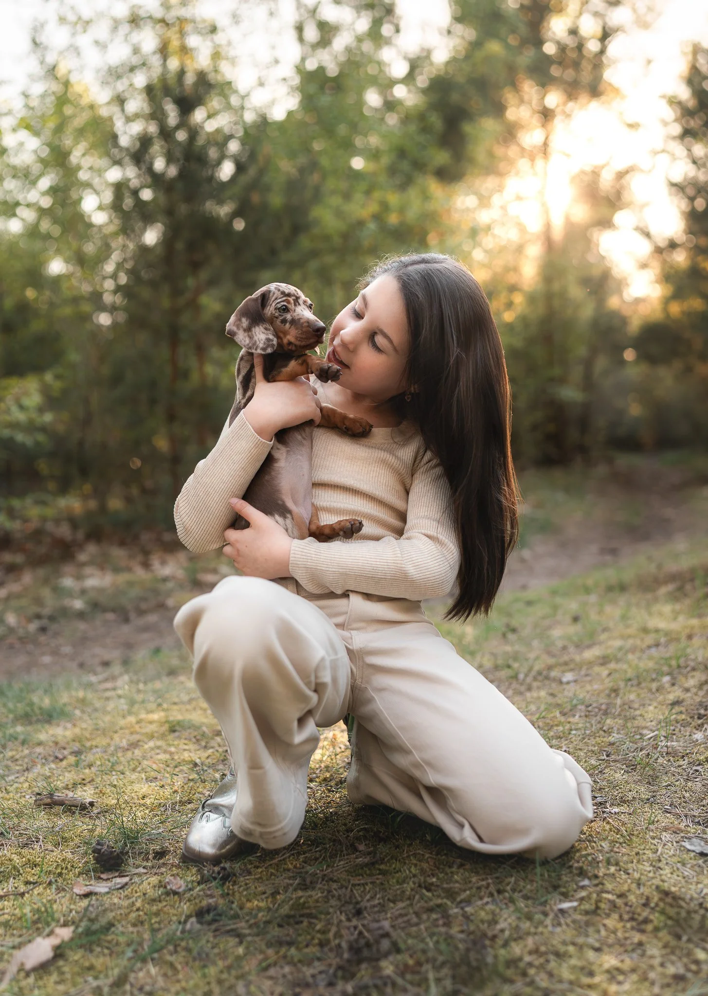 kind die een teckel puppy vasthoudt in een bos tijdens zonsondergang