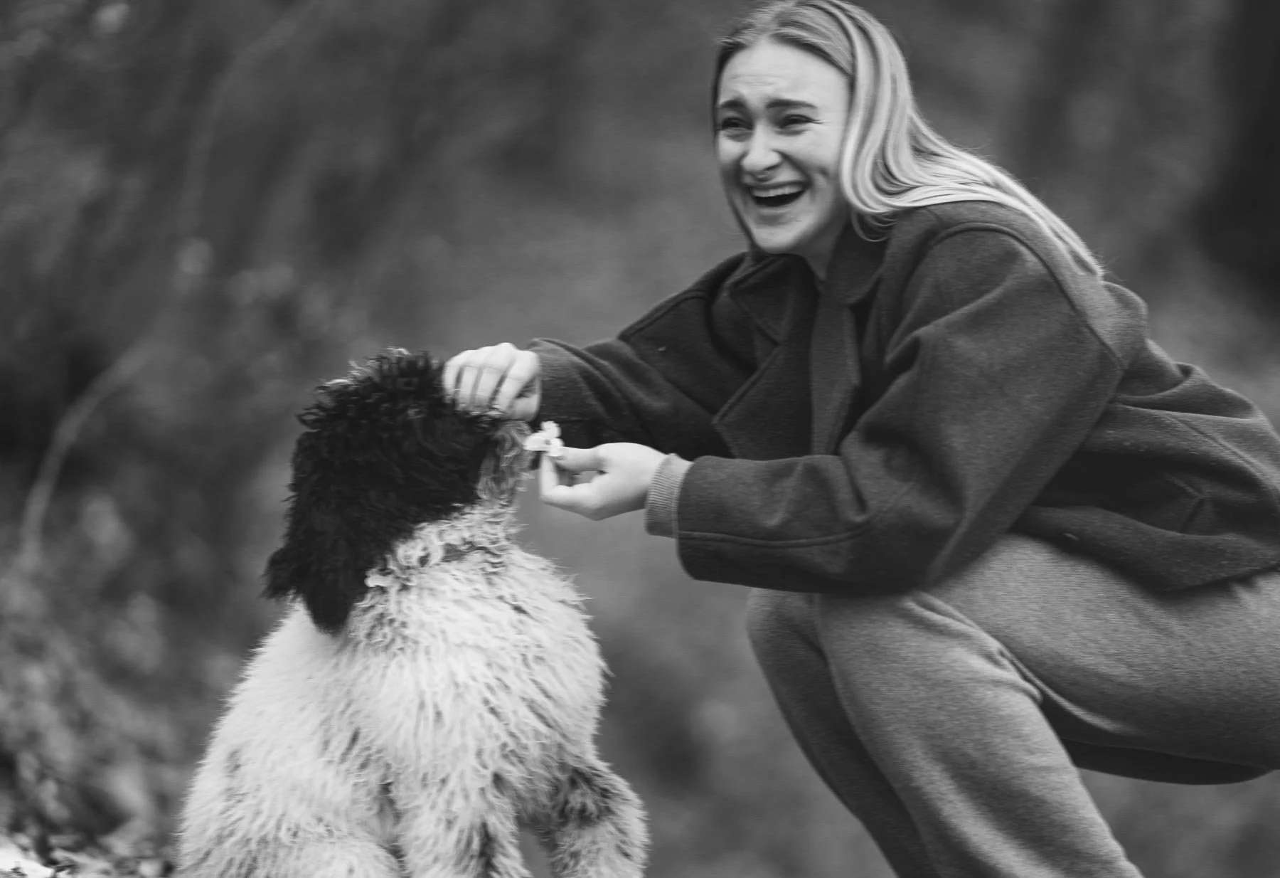 Een vrouw en een hond die samen spelen in een bosrijke omgeving.