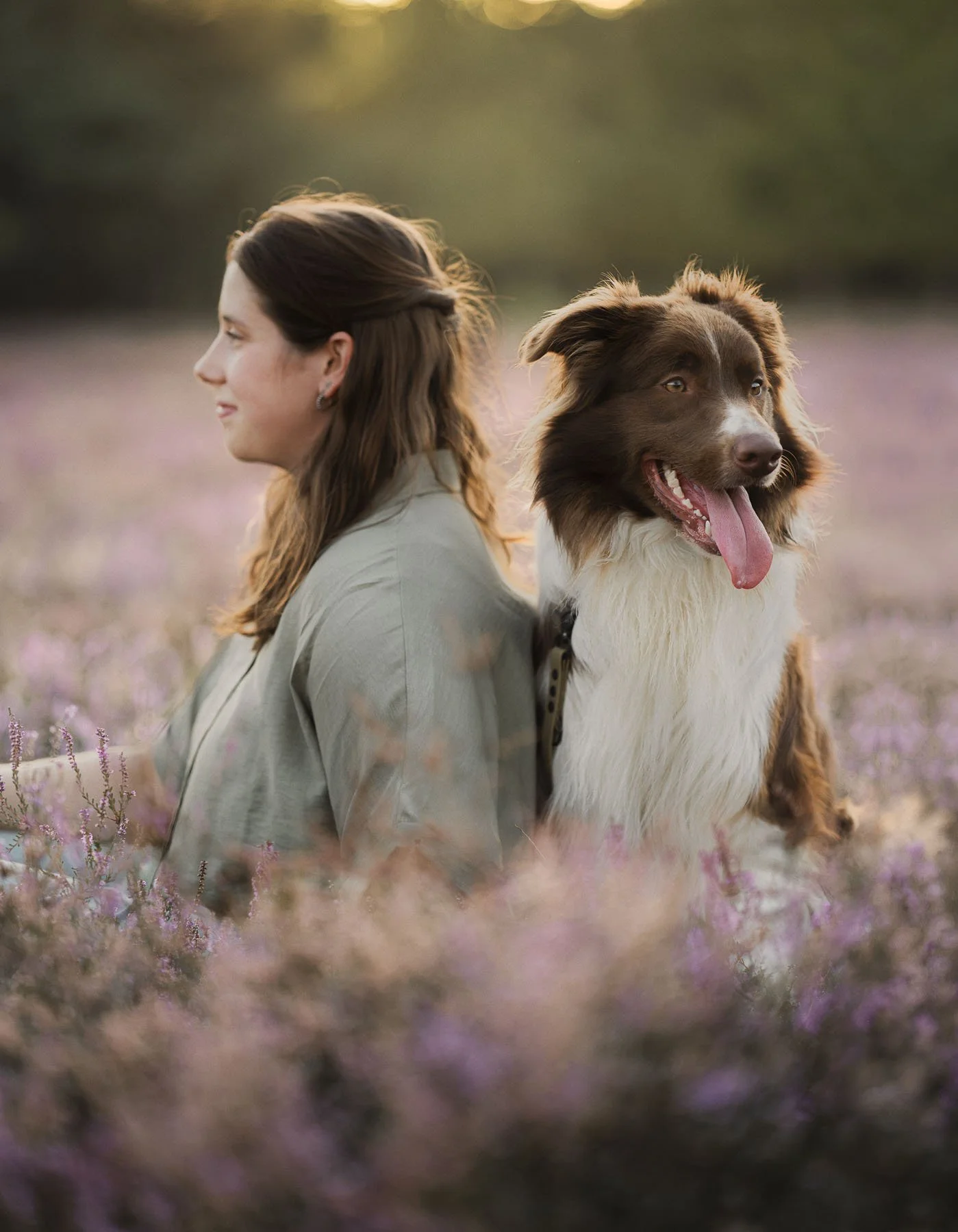 Vrouw en border collie in een veld met bloemen tijdens zonsondergang.
