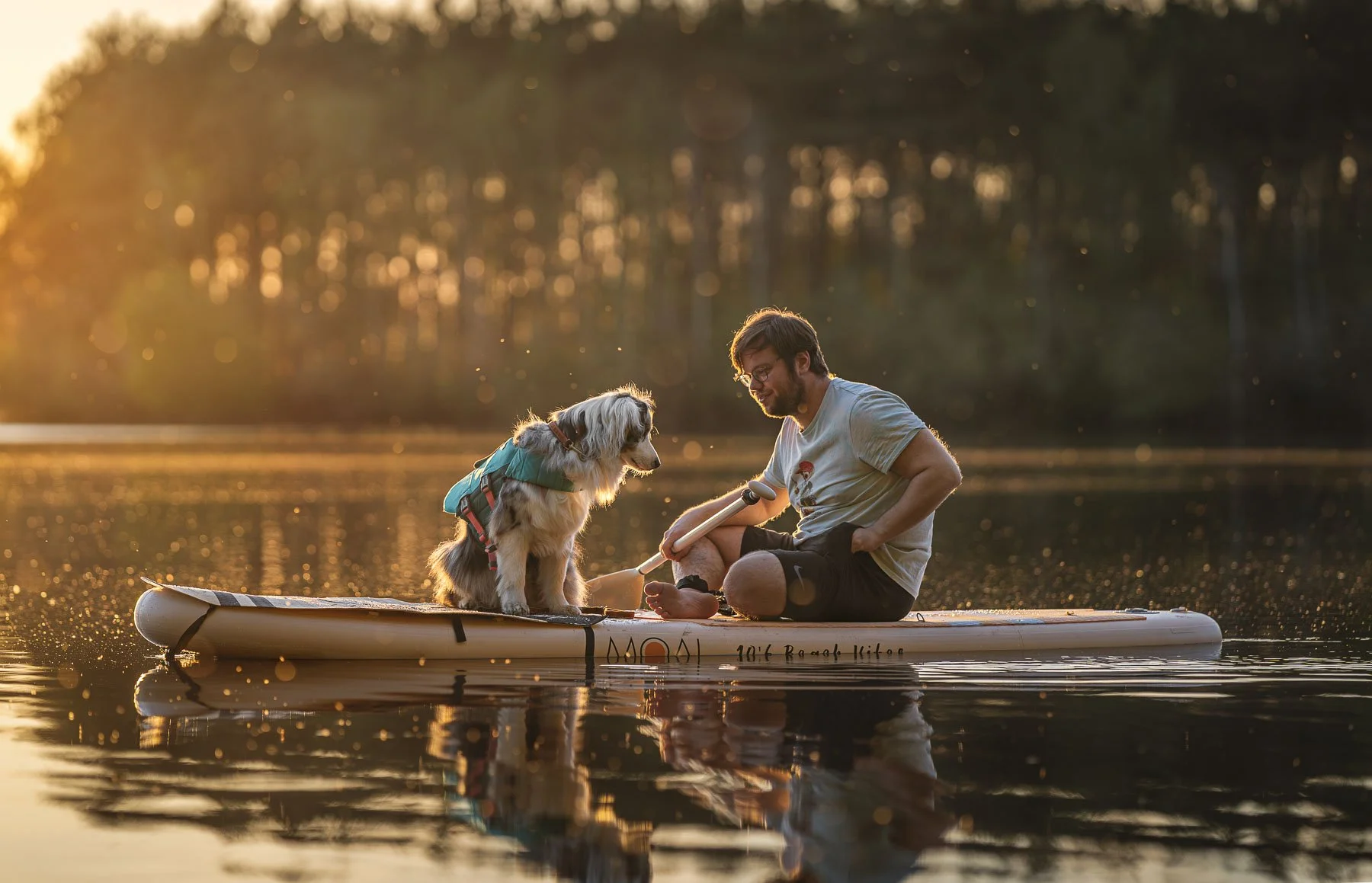 Lifestyle adventure photography featuring a dog and owner on a paddleboard during golden hour