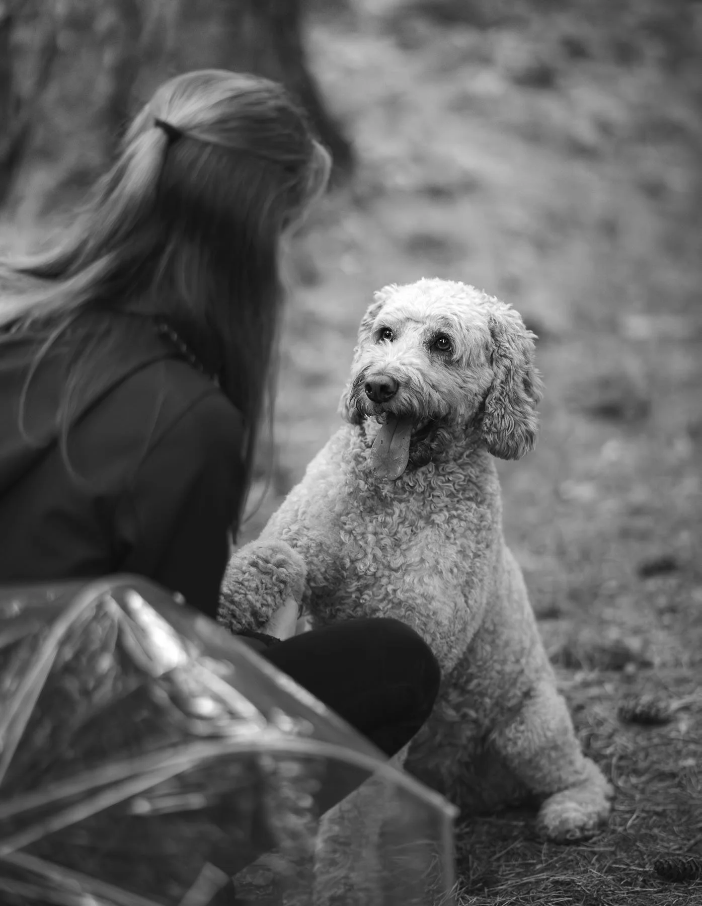 Een persoon met lang haar die een hond aait. Het is zwart-wit, en de hond zit op de grond.