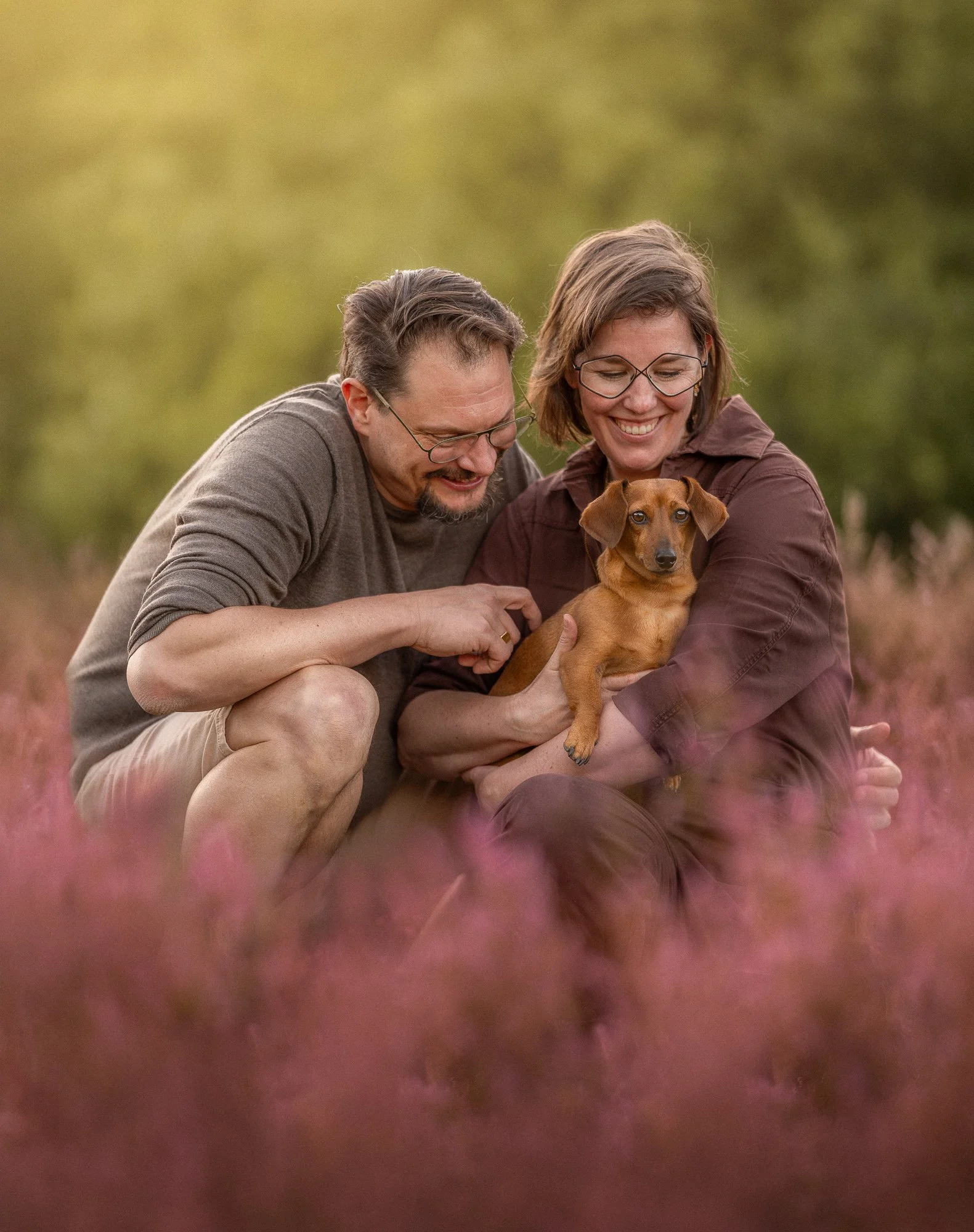 Professionele hondenfotografie van teckel met twee eigenaren in de duinen bij zonsondergang