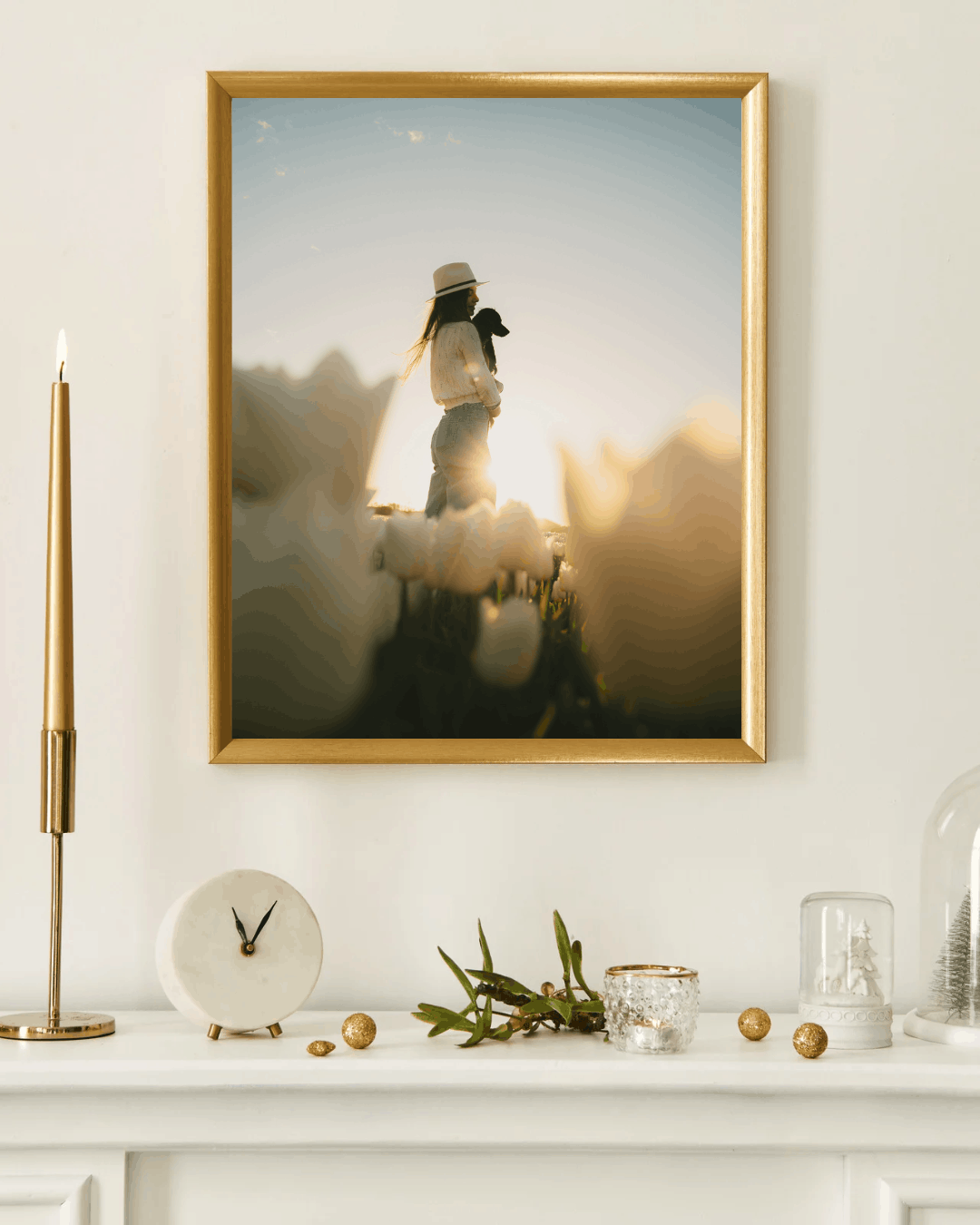 Een foto in een lijst op een muur toont een silhouet van een vrouw met een hoed die een hond vasthoudt, tijdens zonsondergang of zonsopgang, met blurry bloemen op de voorgrond.