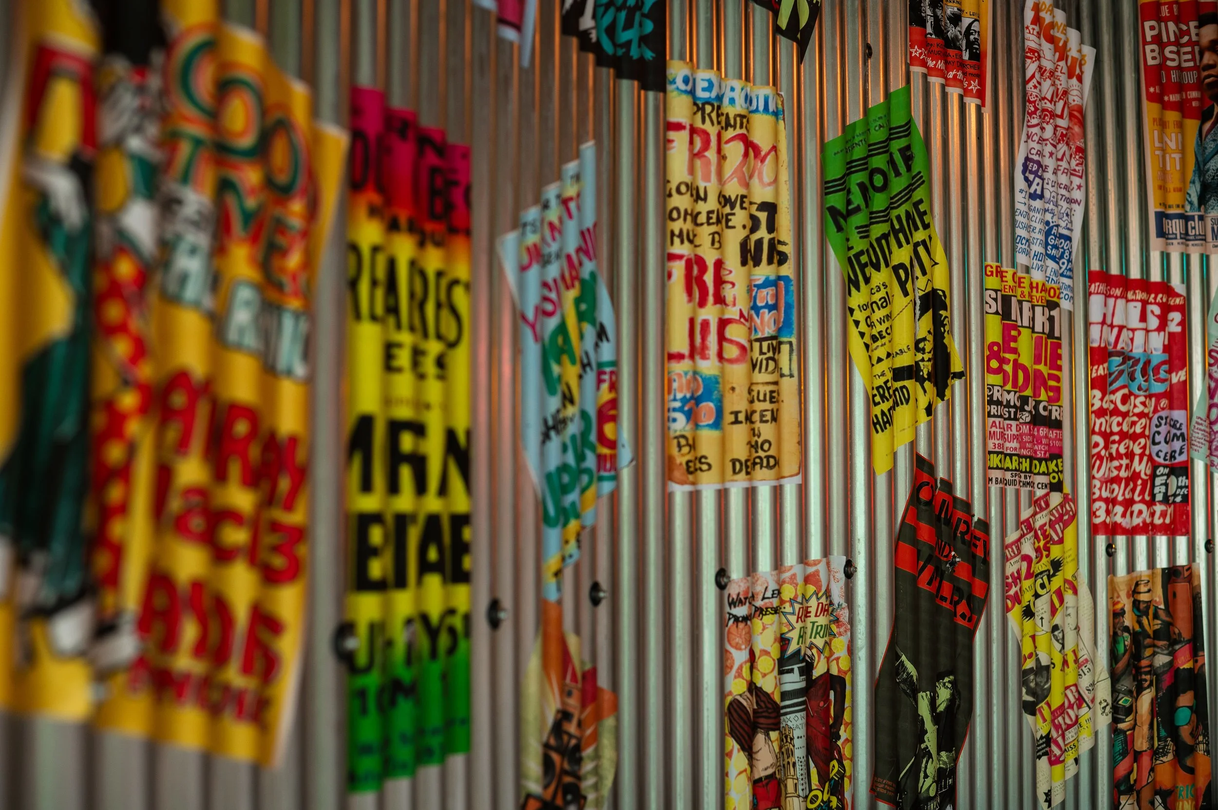 Colorful posters and flyers with various text and images, hanging on vertical silver poles.