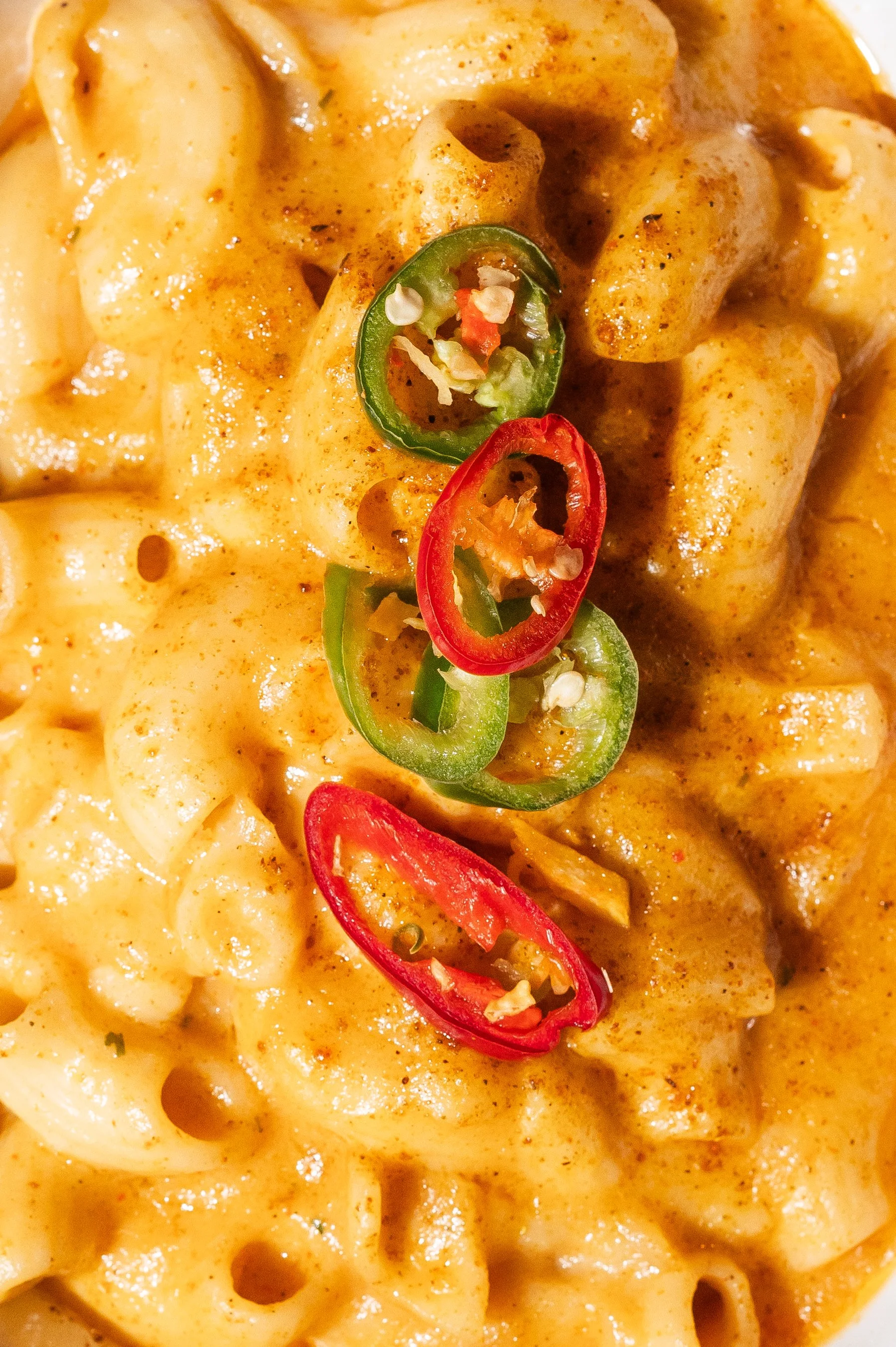 Close-up of macaroni and cheese with sliced red and green chili peppers on top.