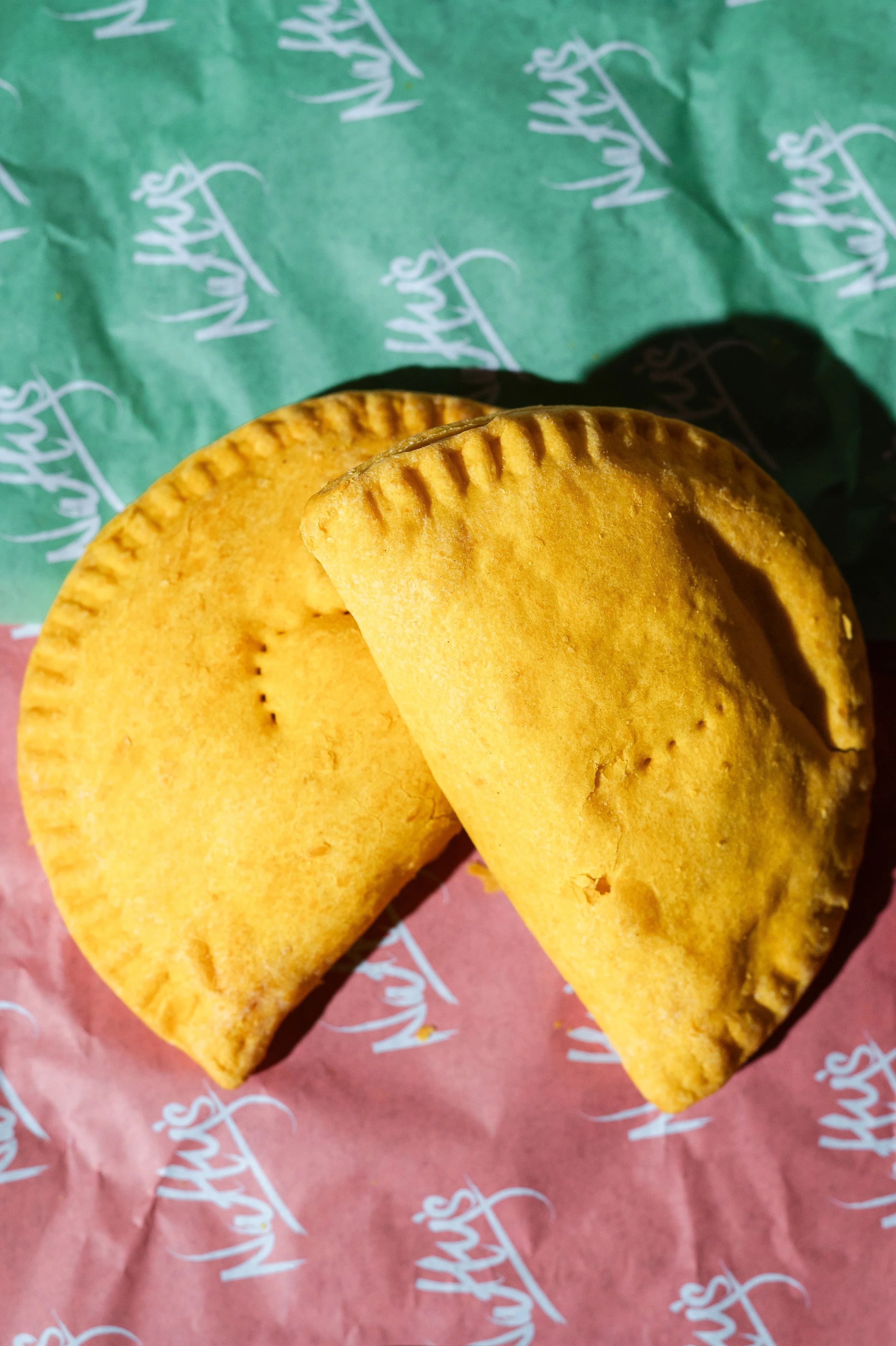 Two golden-brown empanadas on branded red and green paper.