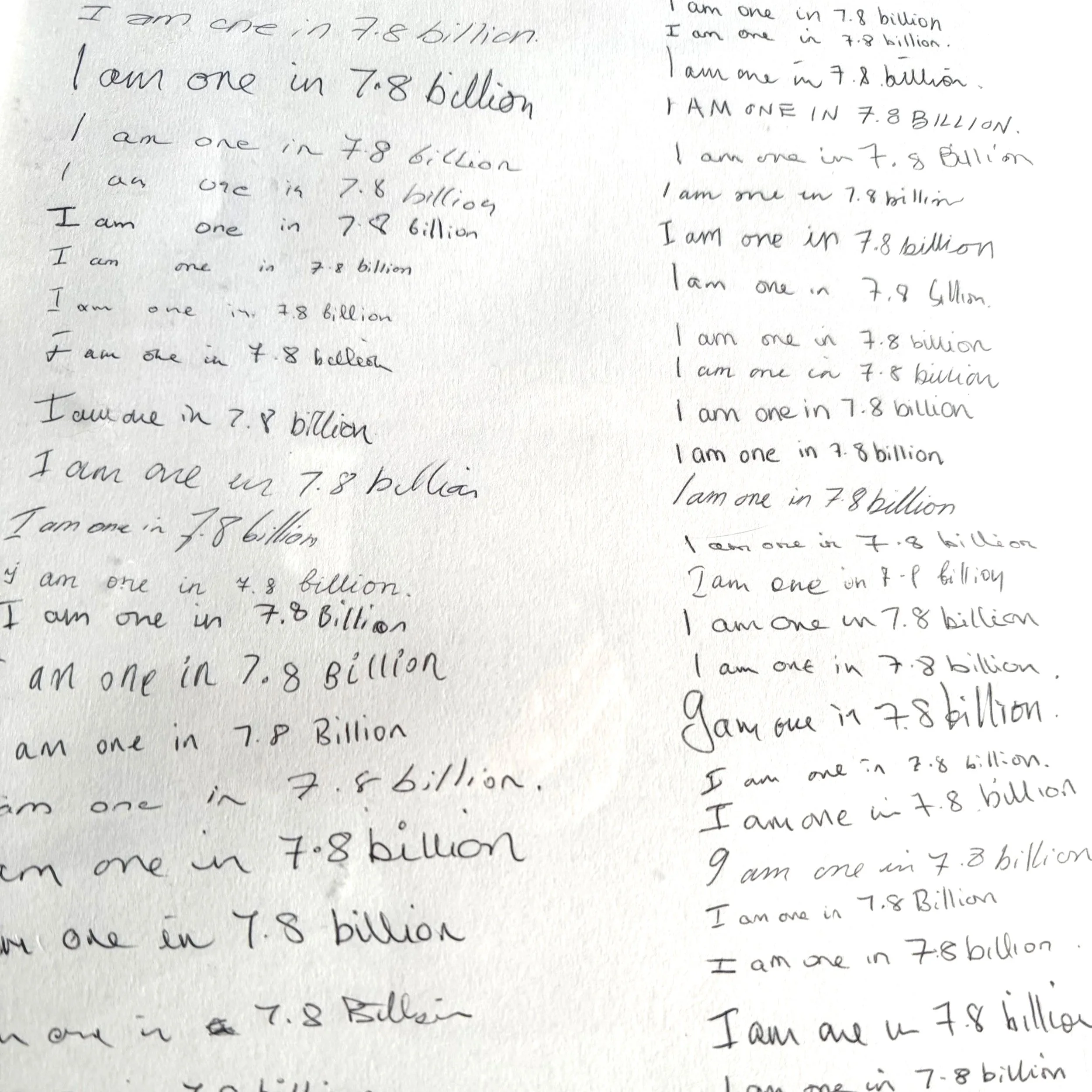 Handwriting samples written in pen on paper of the phrase "I am one in 7.8 billion"