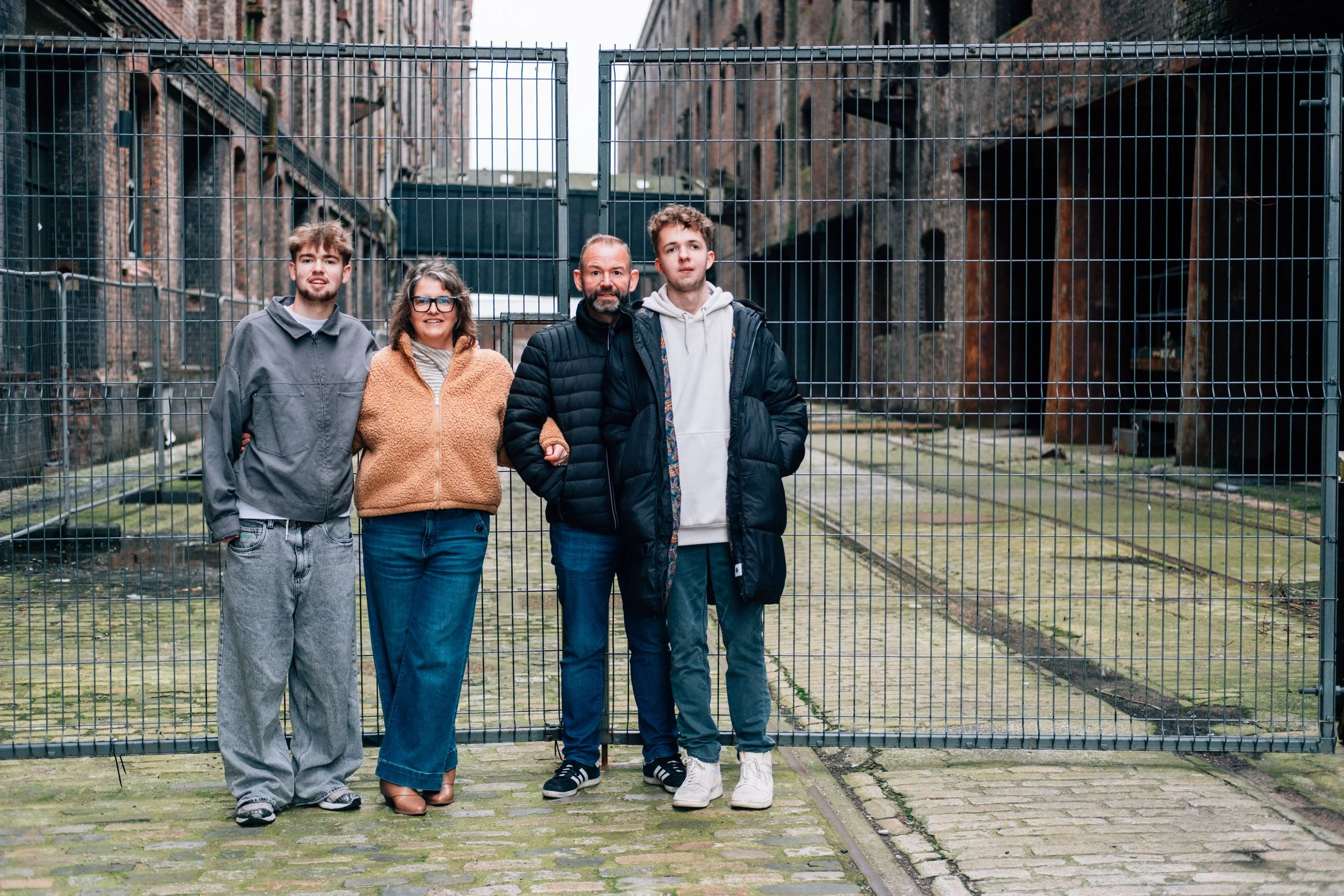 A group of four people standing together in front of a metal gate, with an old brick building in the background.