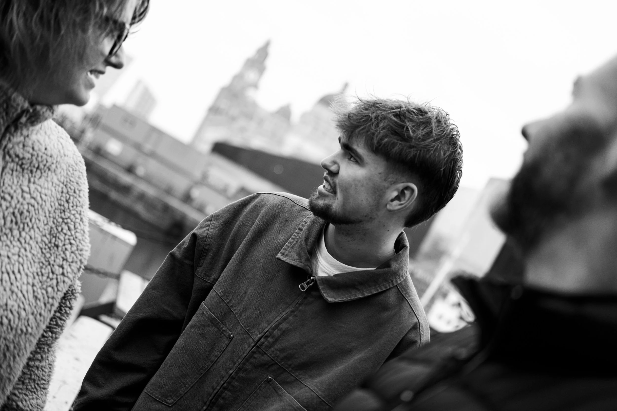 Three people having a conversation outdoors in an urban setting, with blurry buildings in the background. The photo is in black and white.