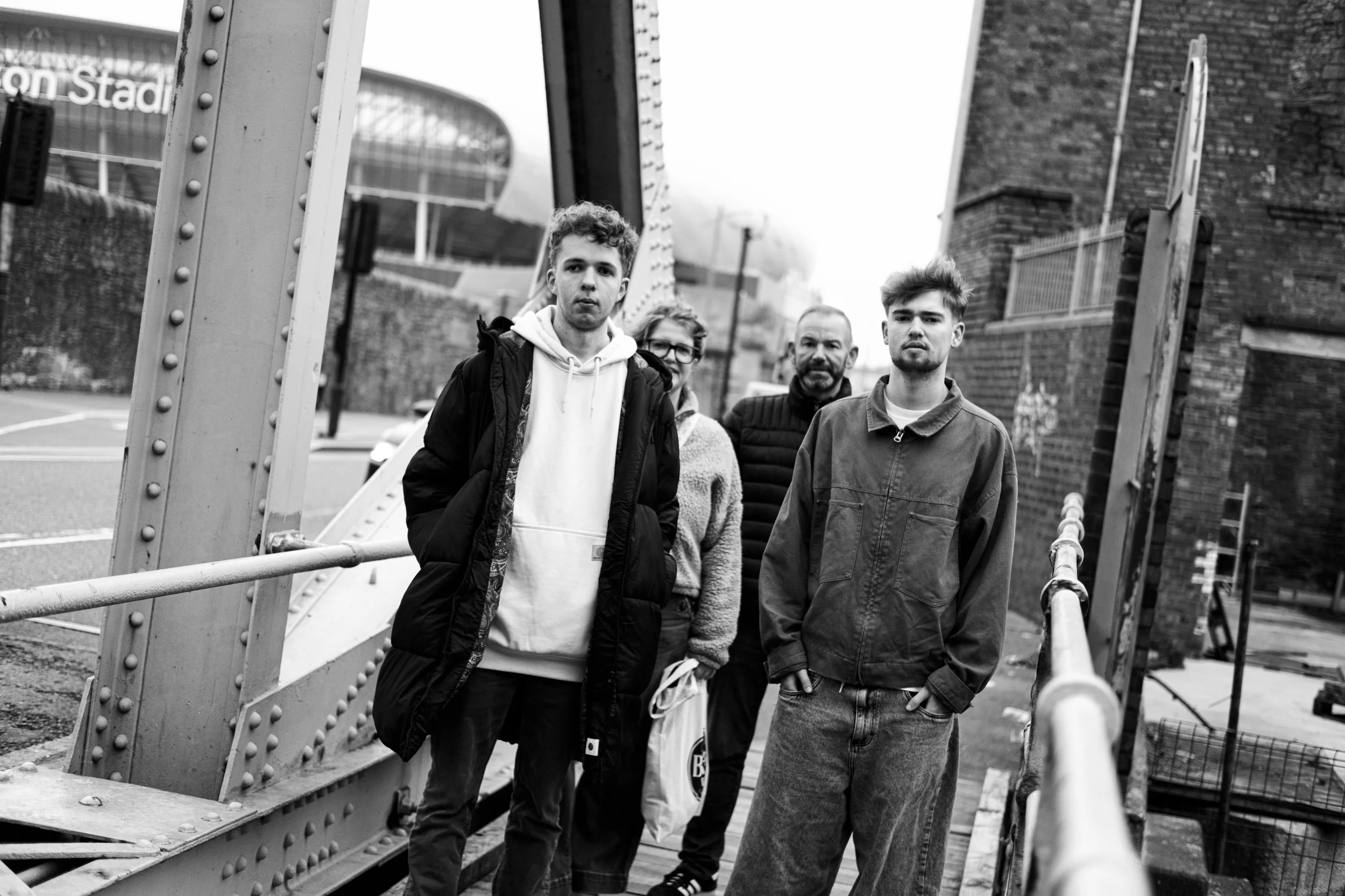 Four people standing on a bridge in an urban environment, black and white photo.