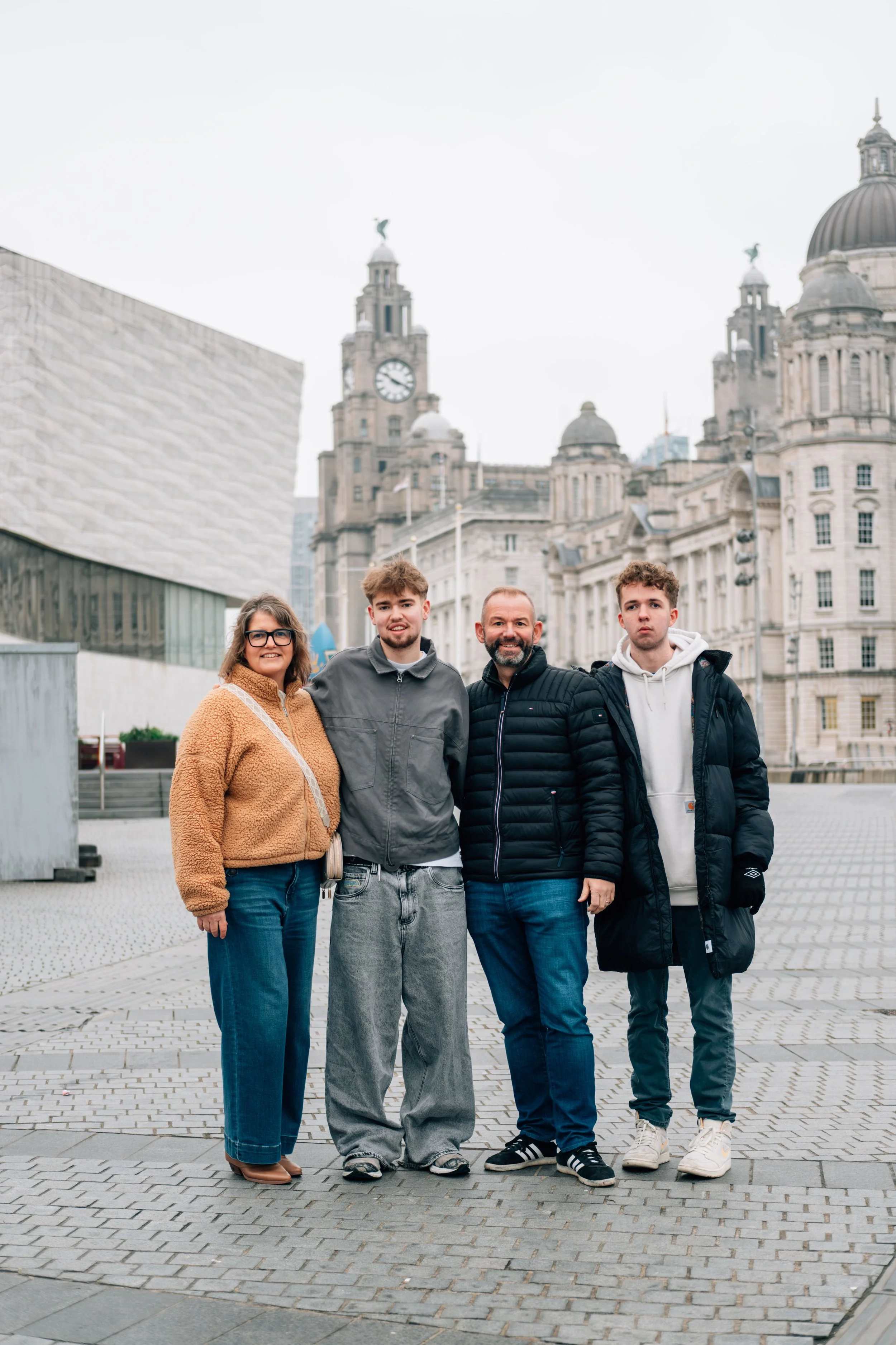 Group of four people smiling and standing together outdoors in front of historic buildings with clock towers and domes.