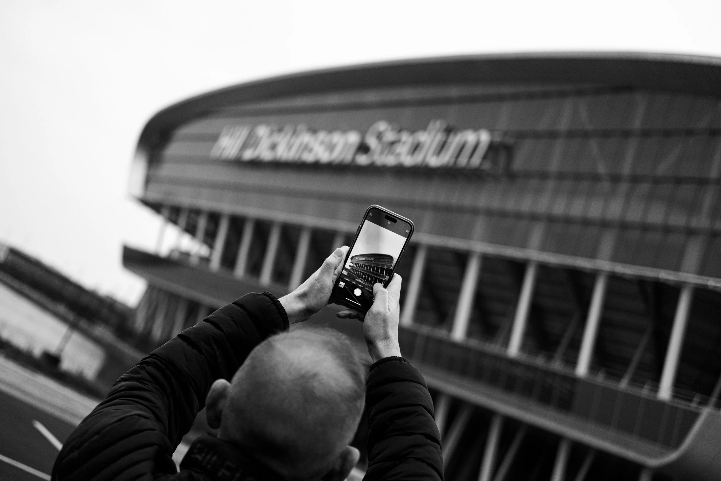 Person taking a photo of Madison Square Garden with a smartphone in black and white.