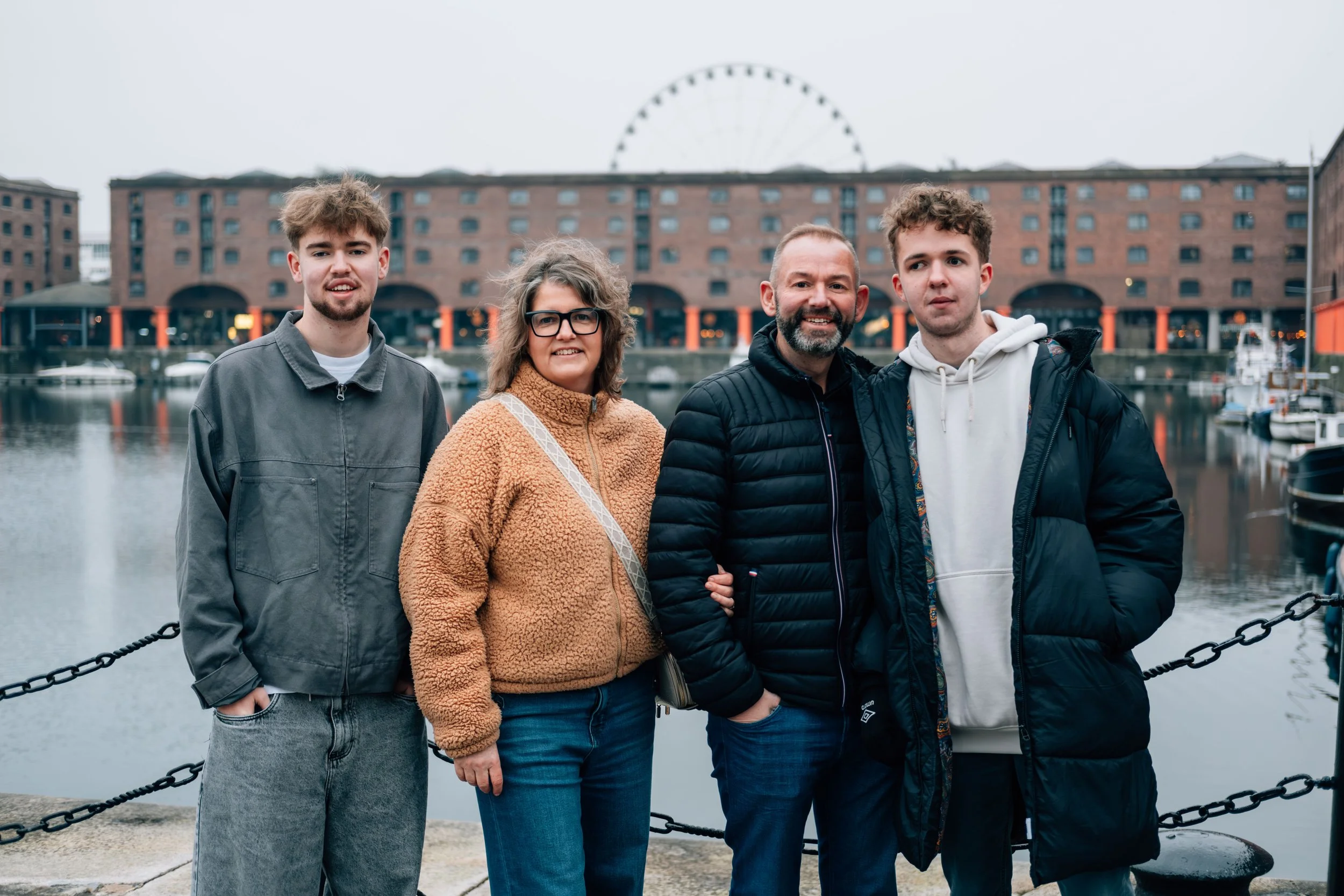 A family of four posing by a harbor with boats and a large building with a Ferris wheel in the background