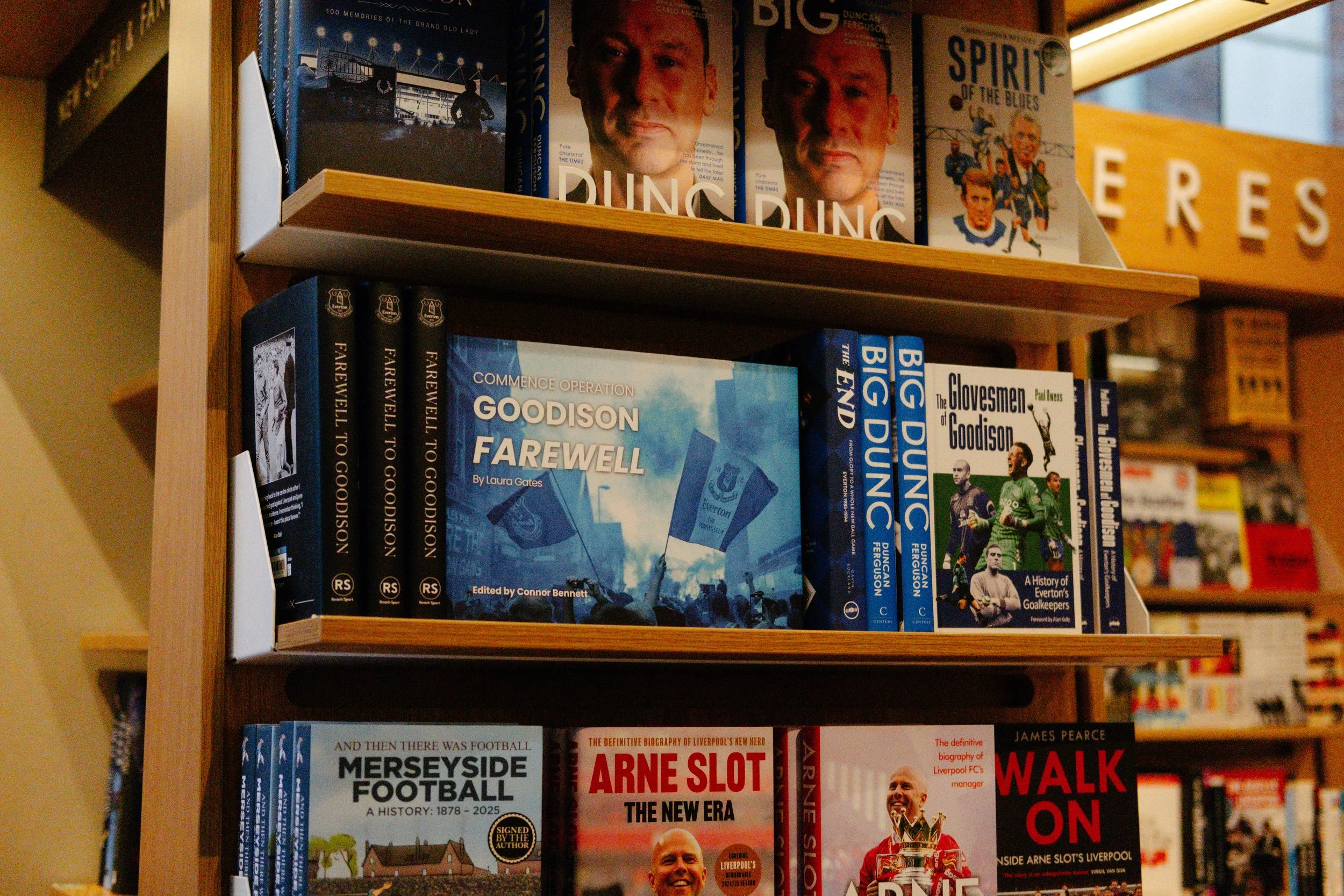 Books about football and Everton FC on a wooden bookshelf, including titles about the history of Everton and football biographies.