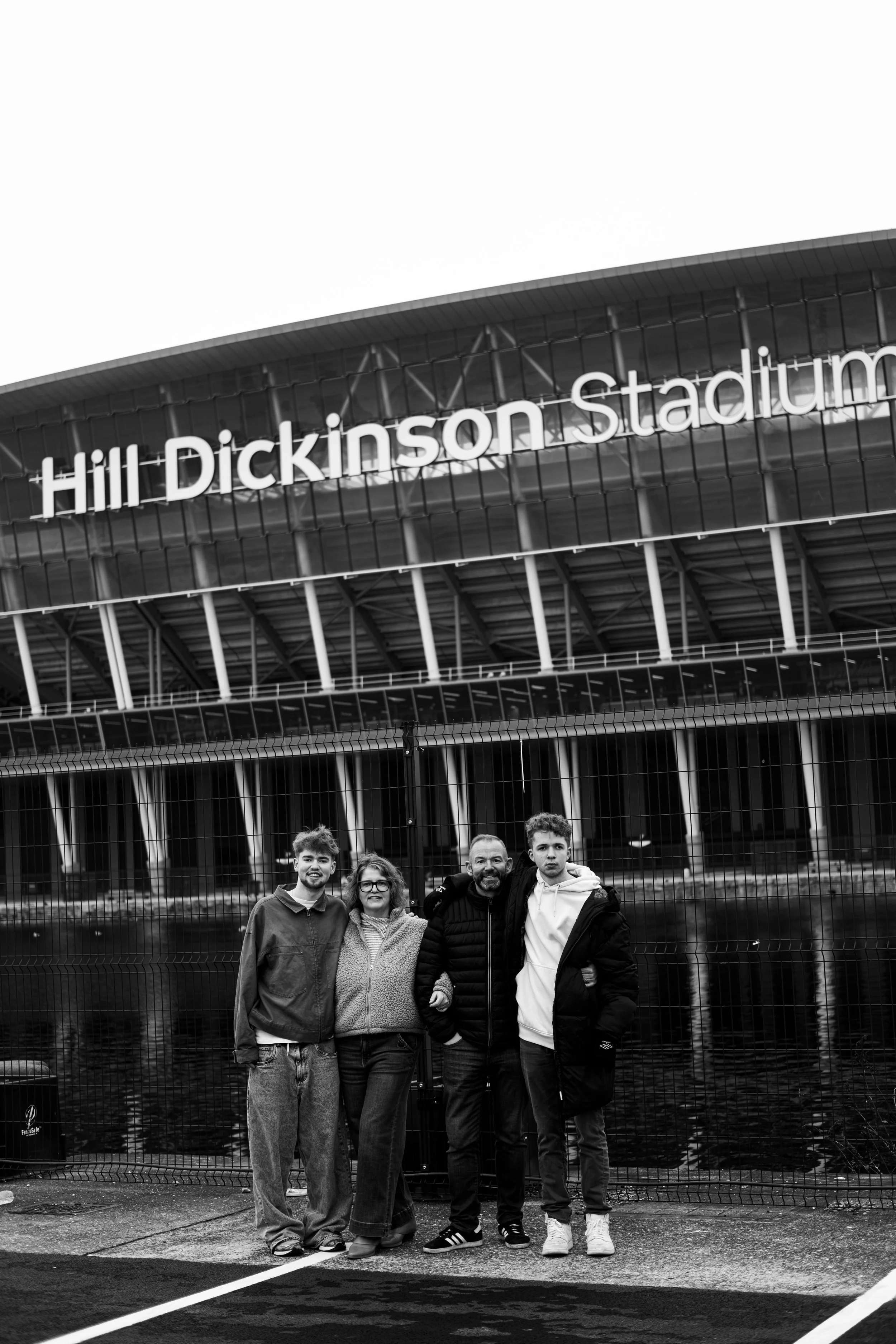 Family of four standing outside in front of the fence near Hill Dickinson Stadium with the stadium in the background.