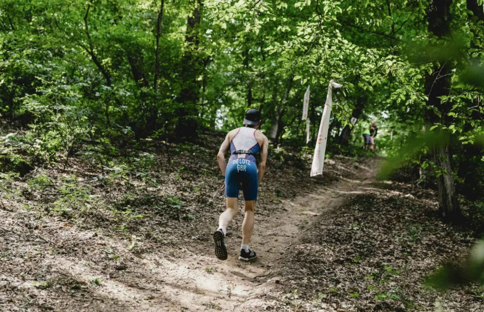 Self-efficacy in endurance training as an athlete runs uphill on a forest trail, building confidence through effort.