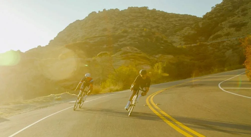 Cyclists riding into a winding road, representing uncertainty and fear of the unknown in long term endurance training.