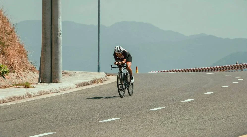 A cyclist riding alone on an open road, representing choosing exposure and engagement over avoidance in endurance training.