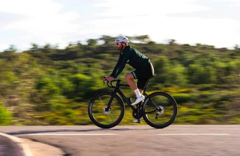 Un cycliste roule à un rythme régulier sur une route dégagée, symbolisant les petites victoires et la concentration mentale.