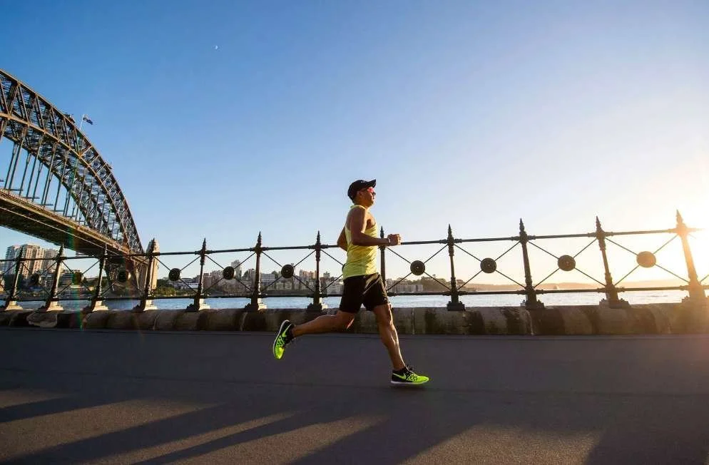 Runner training at sunrise near Sydney Harbour Bridge representing marathon endurance workouts.