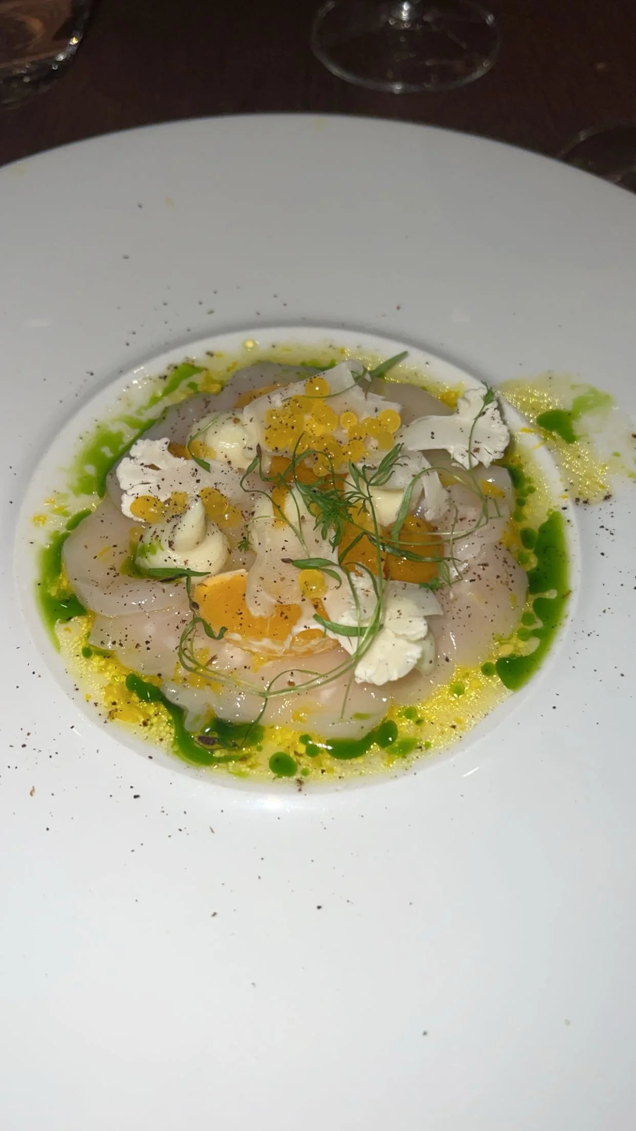 Assiette de carpaccio de poisson garnie de crème, œufs de poisson, herbes et sauce verte.