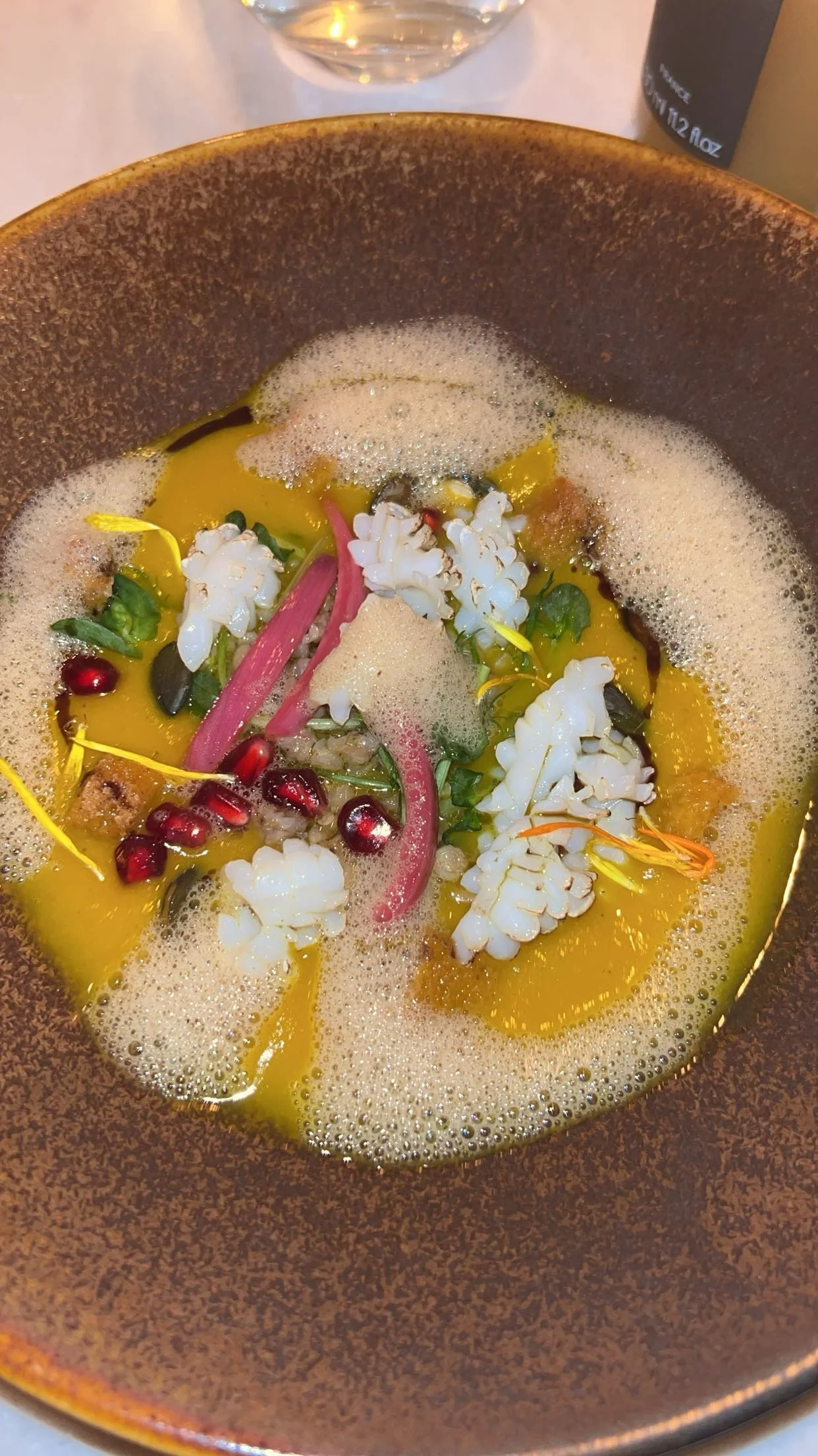 Soupe avec des grains de riz, des graines de grenade, des fleurs, des légumes et des bulles.