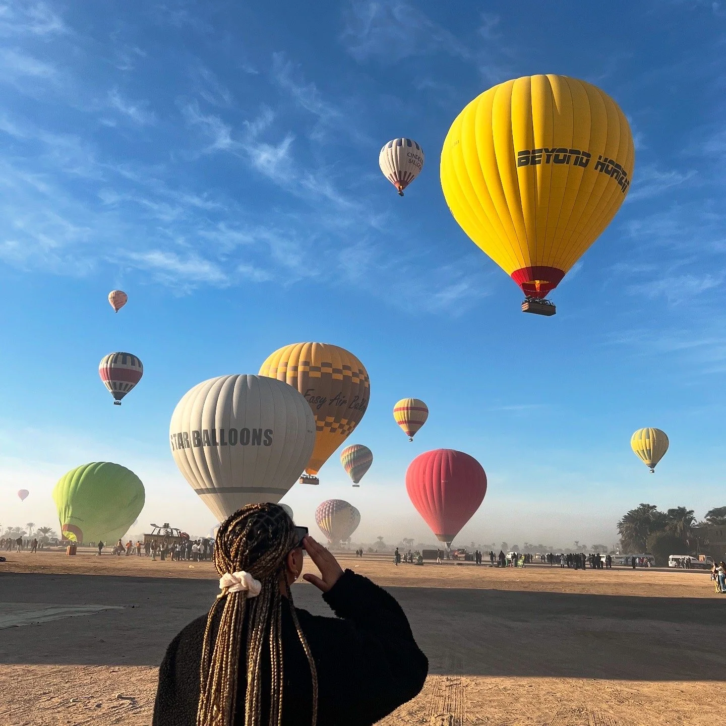Une femme regarde des ballons à air chaud colorés s'élever dans un ciel bleu lors d'un festival de montgolfières.