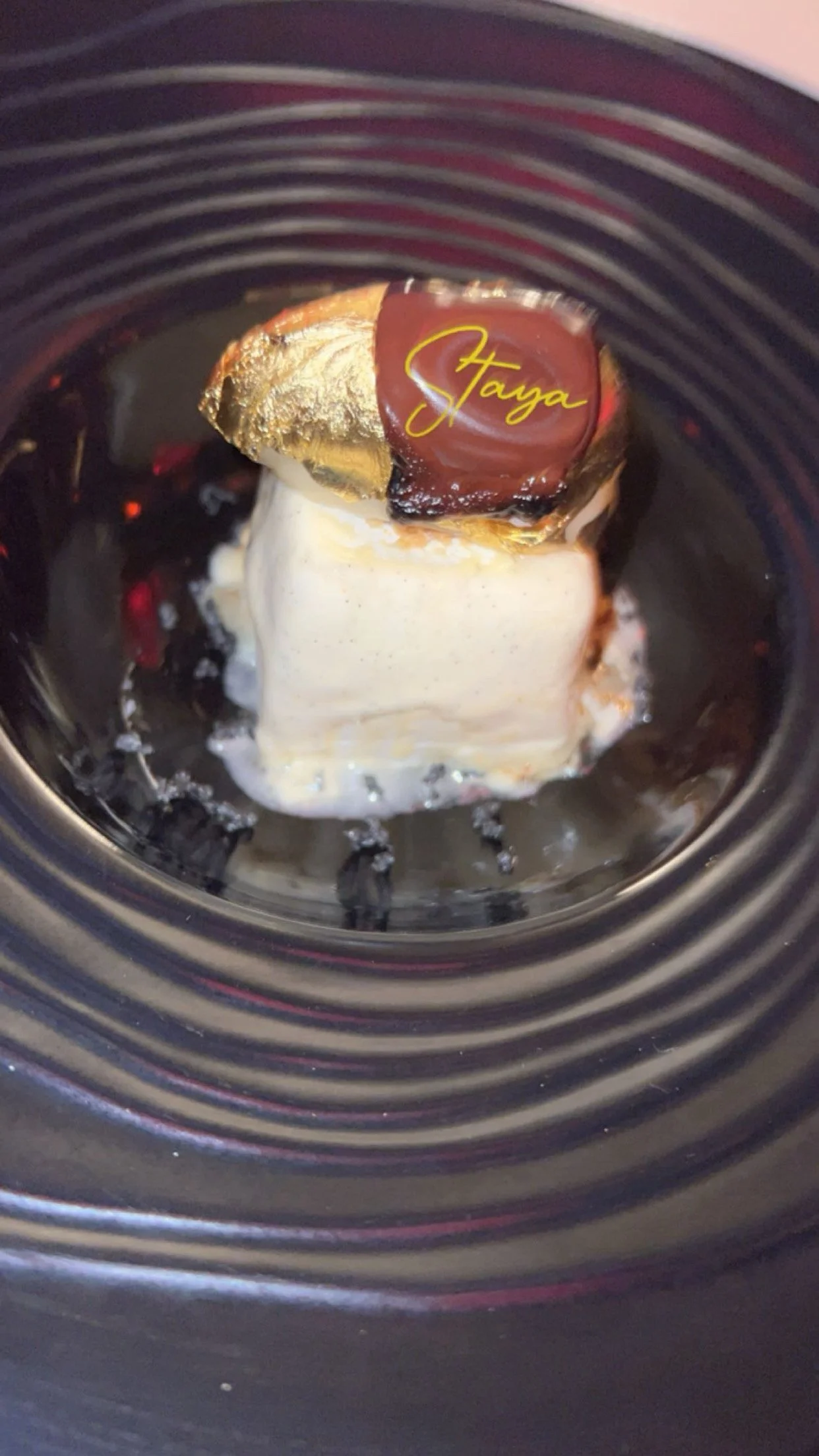 Dessert glacé, probablement une glace avec un topping en chocolat, présenté dans un bol noir avec des rayures concentriques.