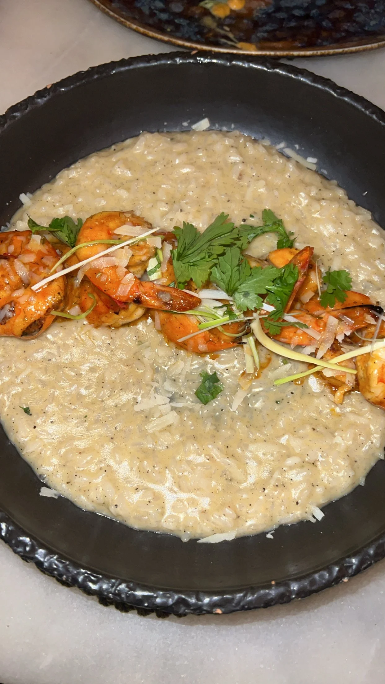 Un plat de risotto crémeux avec des crevettes garnies de coriandre et de microgreens.