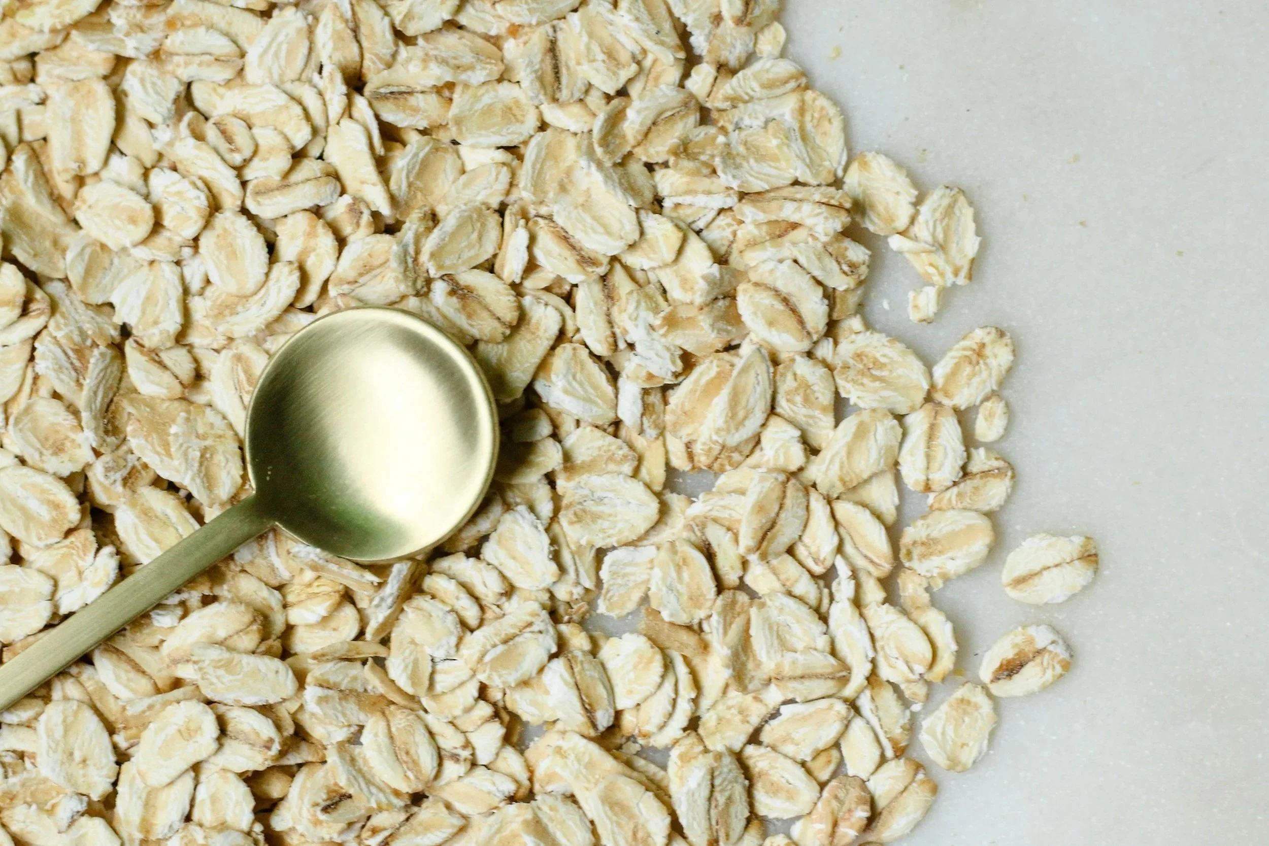 Close-up of rolled oats with a metal measuring spoon on a light surface.