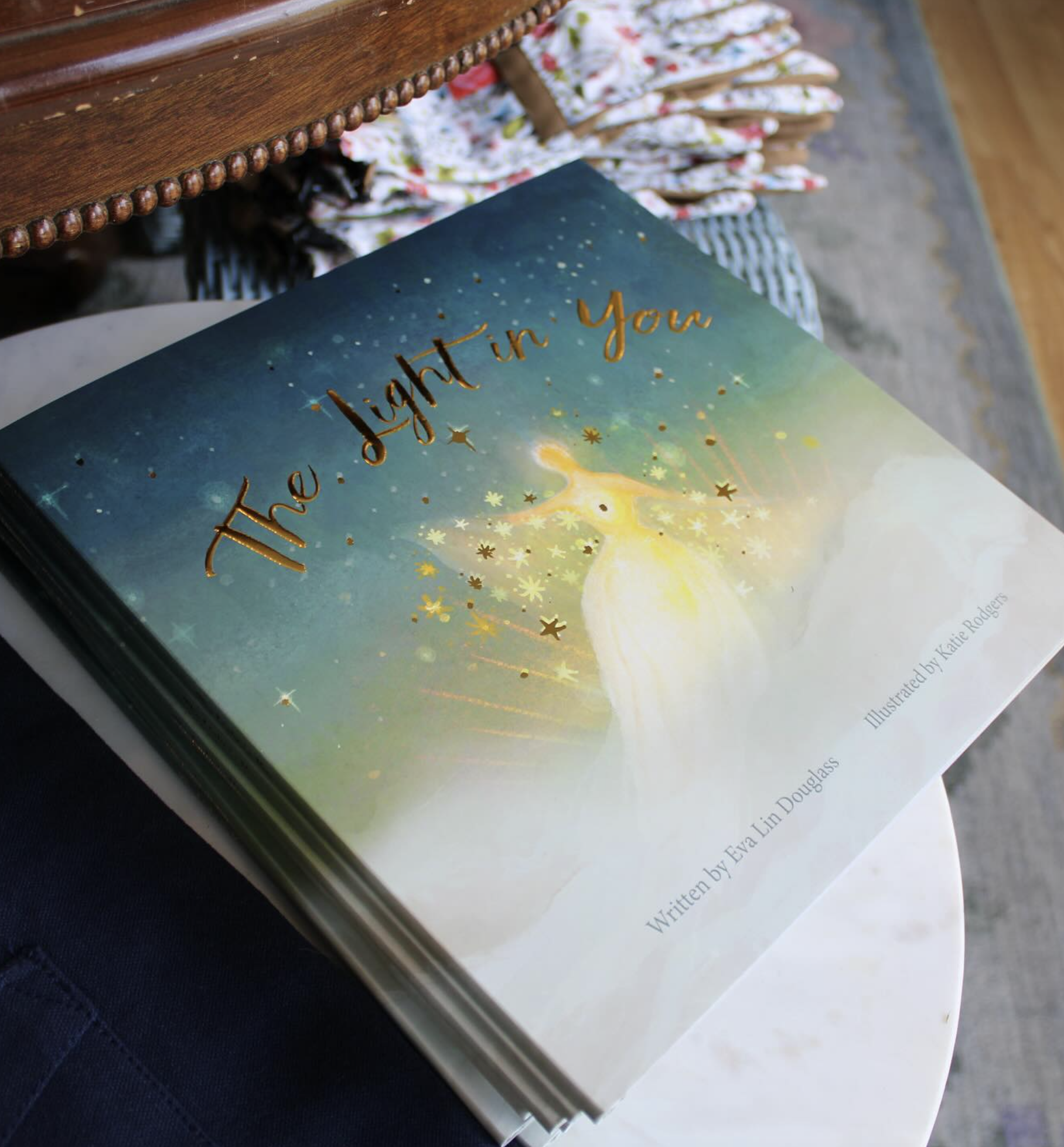 A children's book titled 'The Light in You' resting on a white table, with a dark blue background and an illustration of a glowing fairy surrounded by stars on the cover.