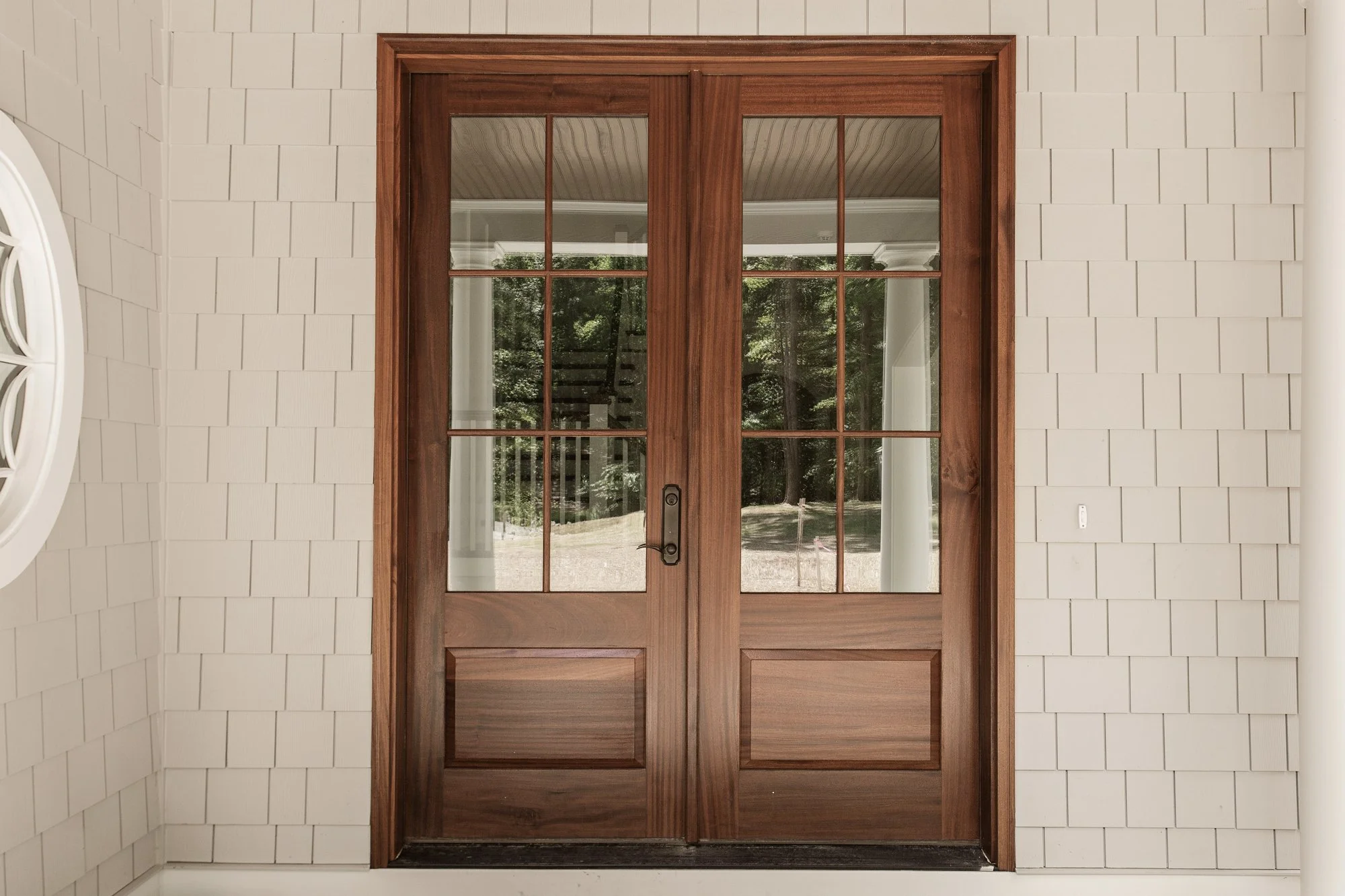 Wooden double door with glass panels in a white shingled exterior wall.