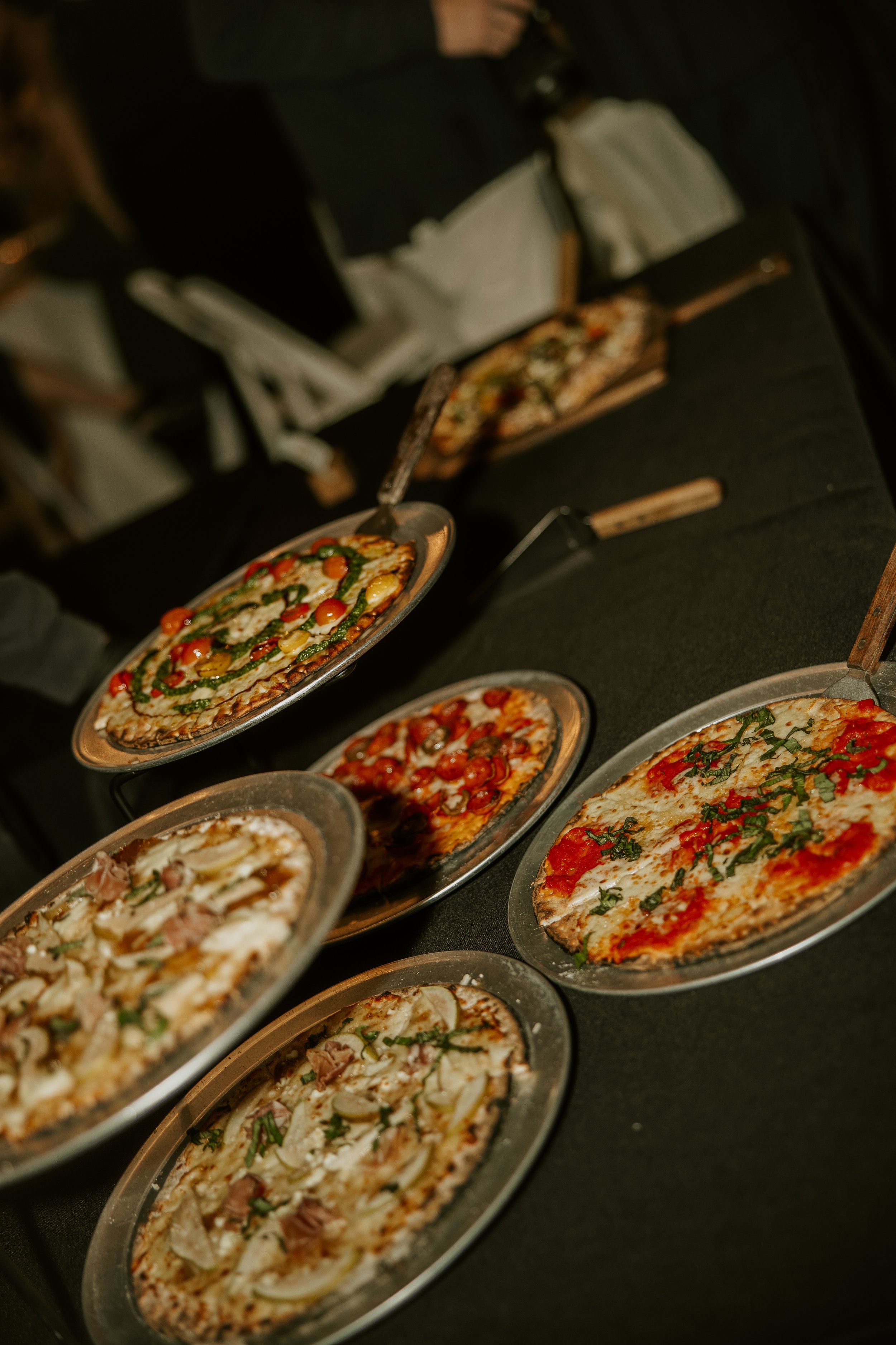 Multiple pizzas with various toppings displayed on a black table at a pizza event.