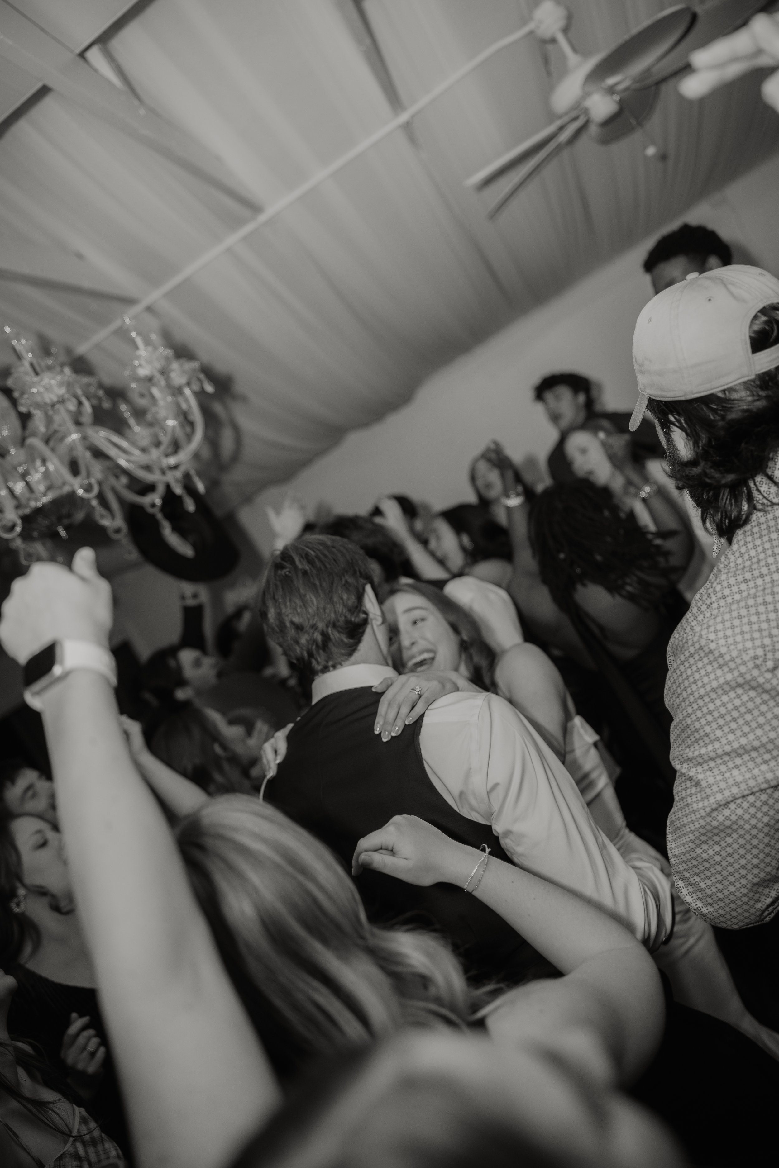 People dancing and celebrating at a party or wedding reception with a chandelier hanging from the ceiling.