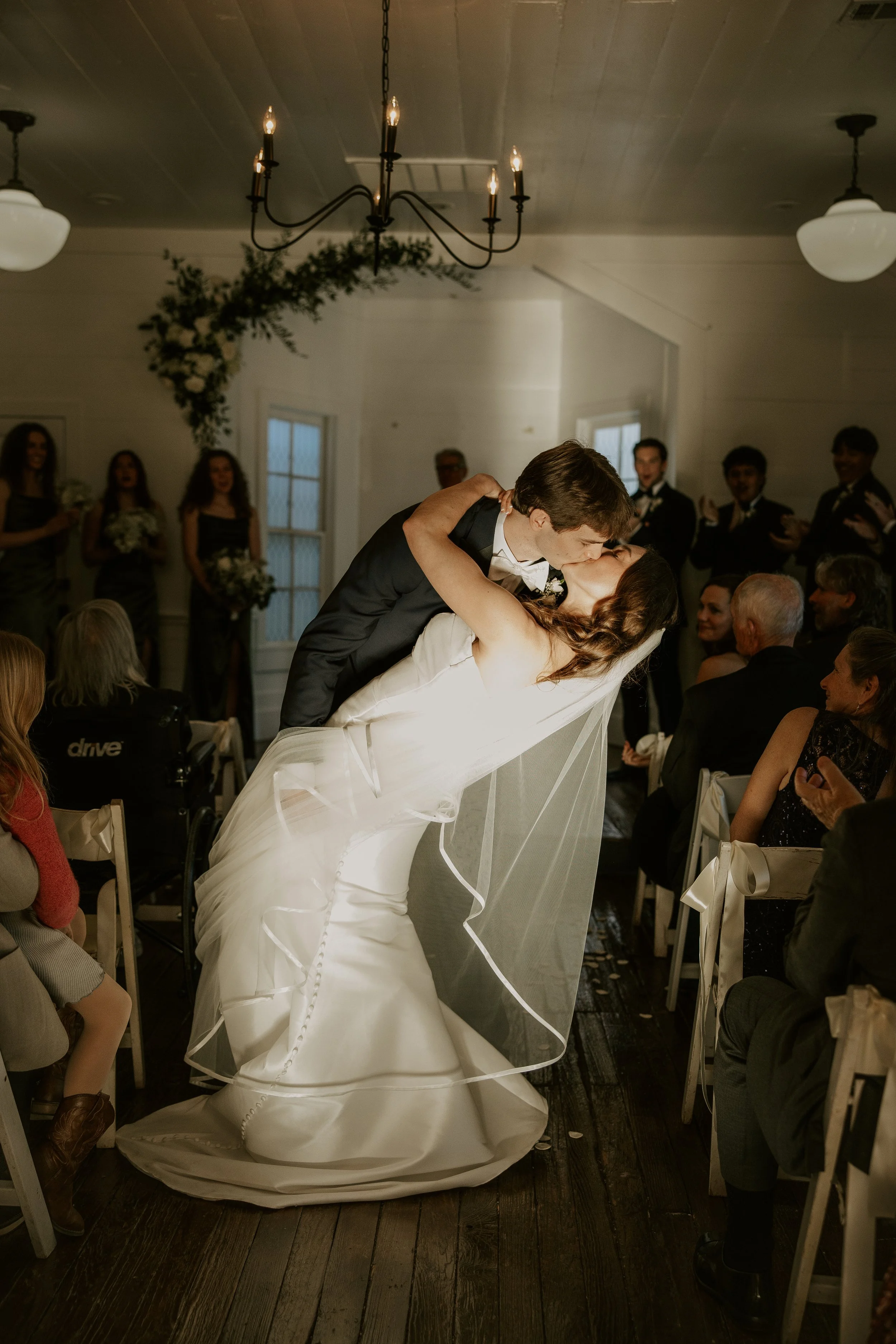 A bride and groom sharing a kiss, with the groom dipping the bride during their wedding reception in a decorated indoor venue.