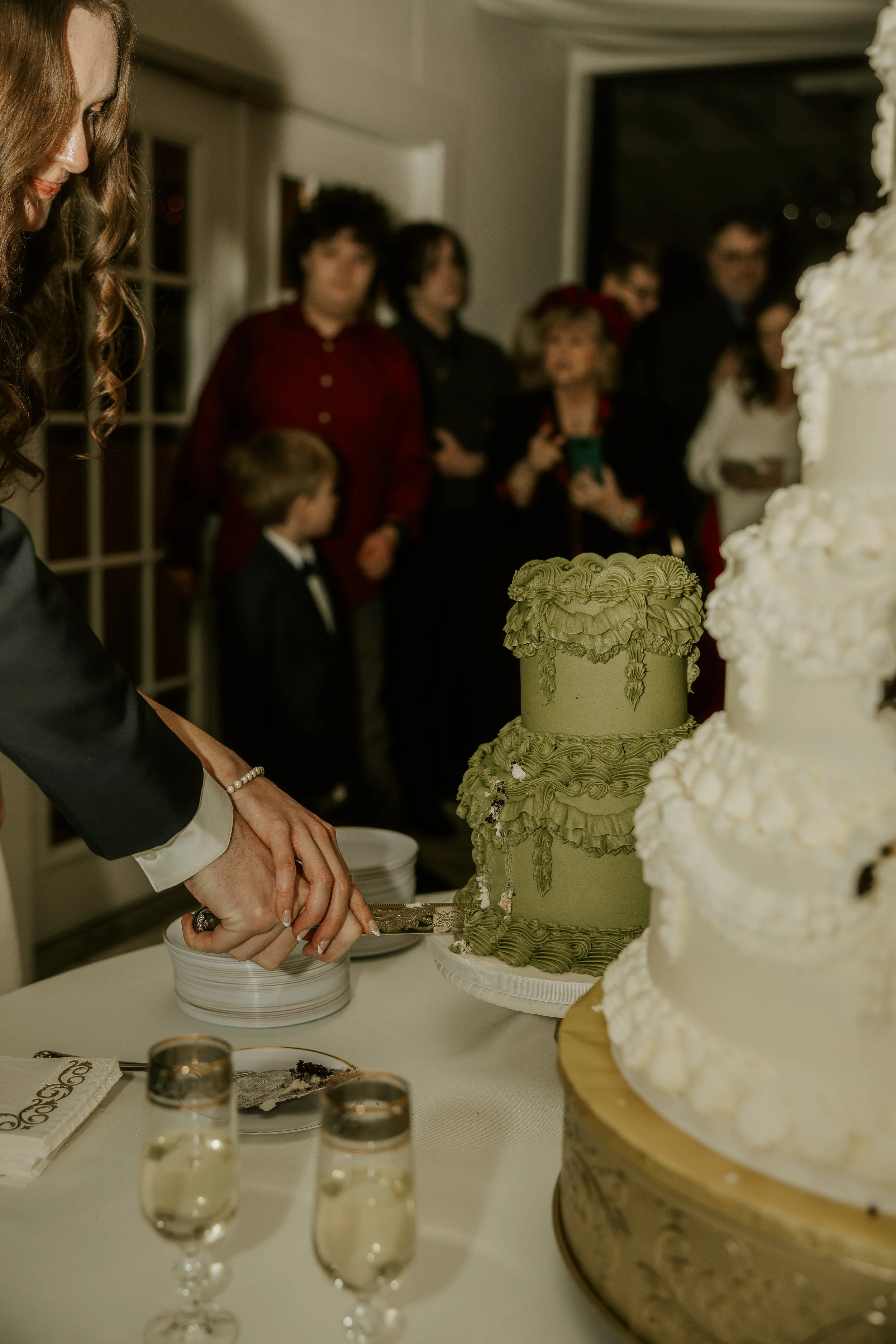 People cutting a wedding cake at the reception, with a layered cake, glasses of champagne, and guests watching.