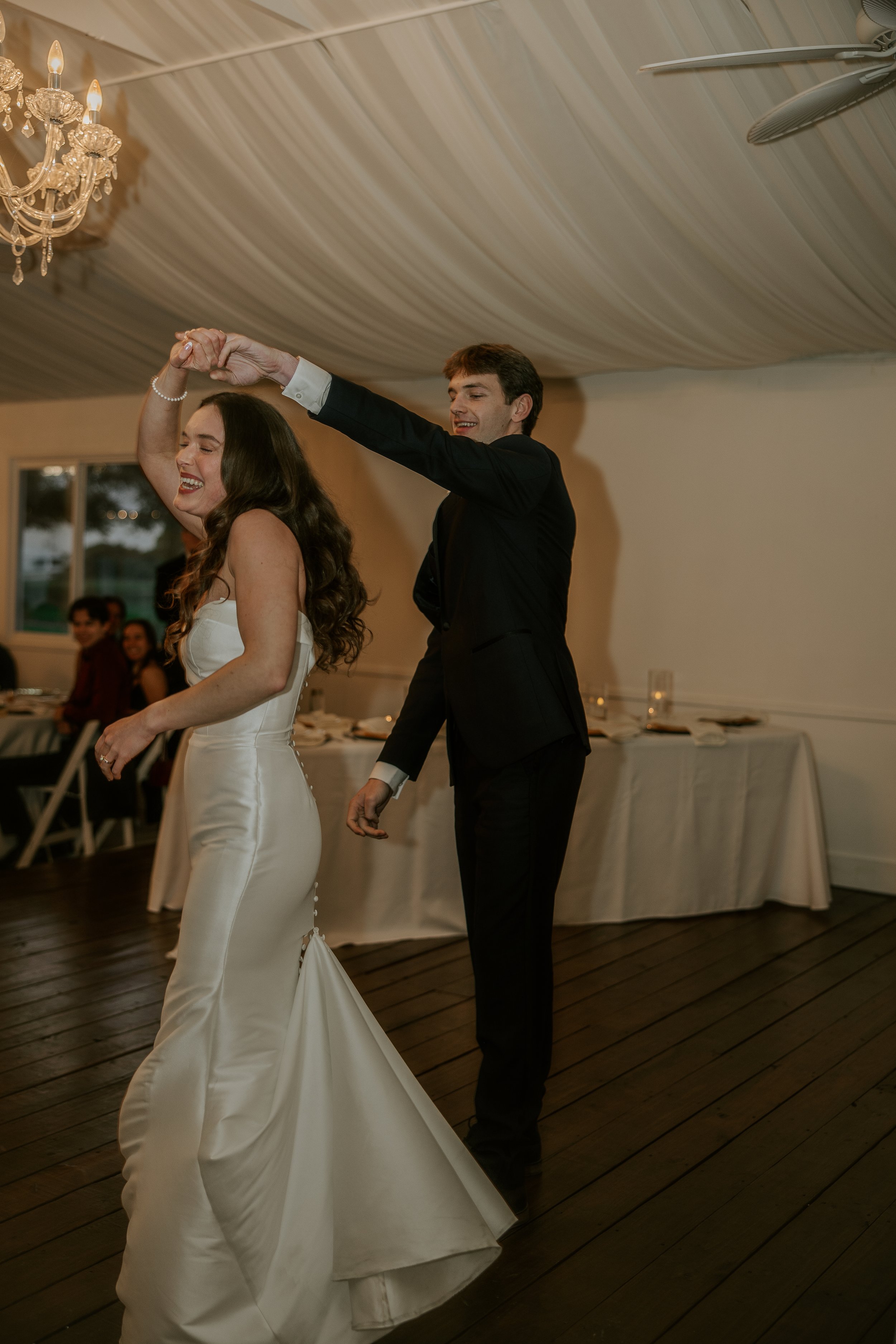 A bride and groom dancing together at their wedding reception, holding hands with the groom twirling the bride.