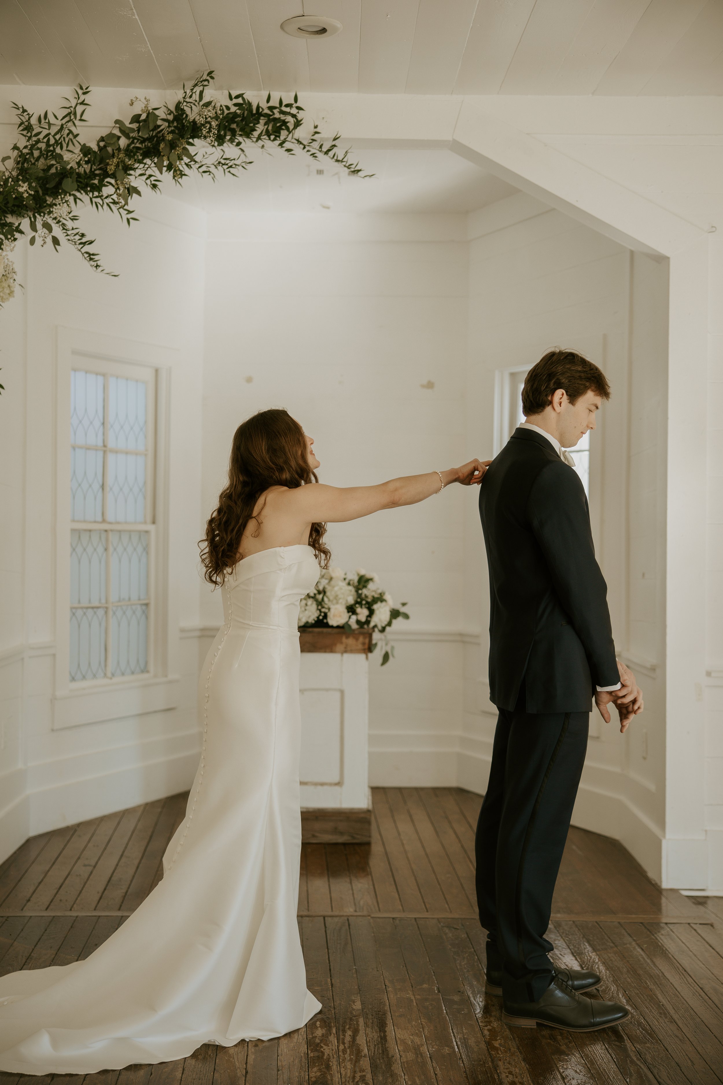 A bride tugging at the groom's tuxedo in a wedding ceremony setting.