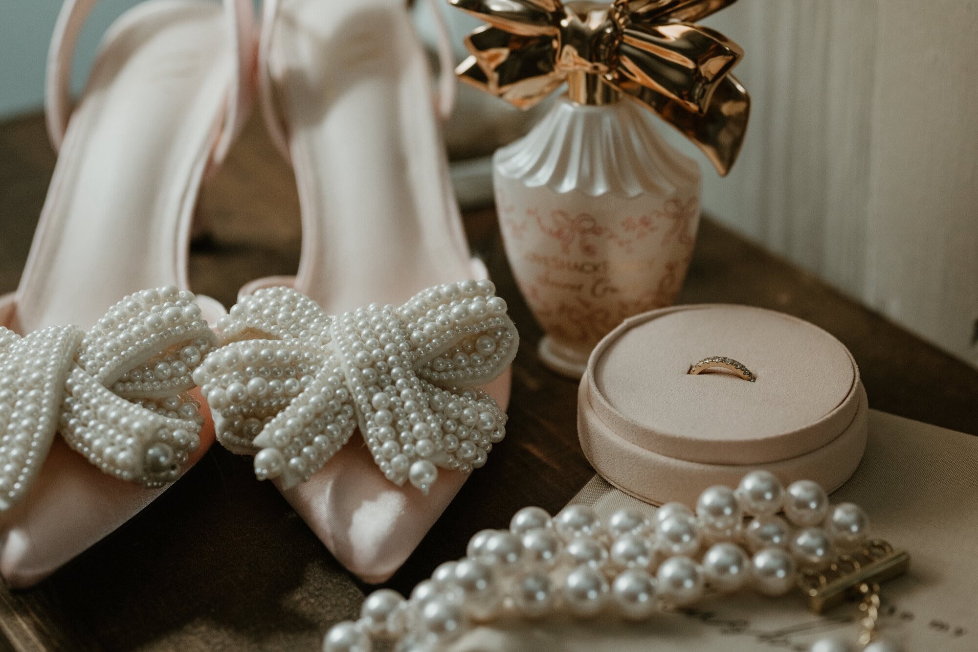 A collection of pearl jewelry including a pearl bracelet, a pearl hair bow, and a pearl necklace, along with a gold ring in a pink ring box, placed on a wooden surface.
