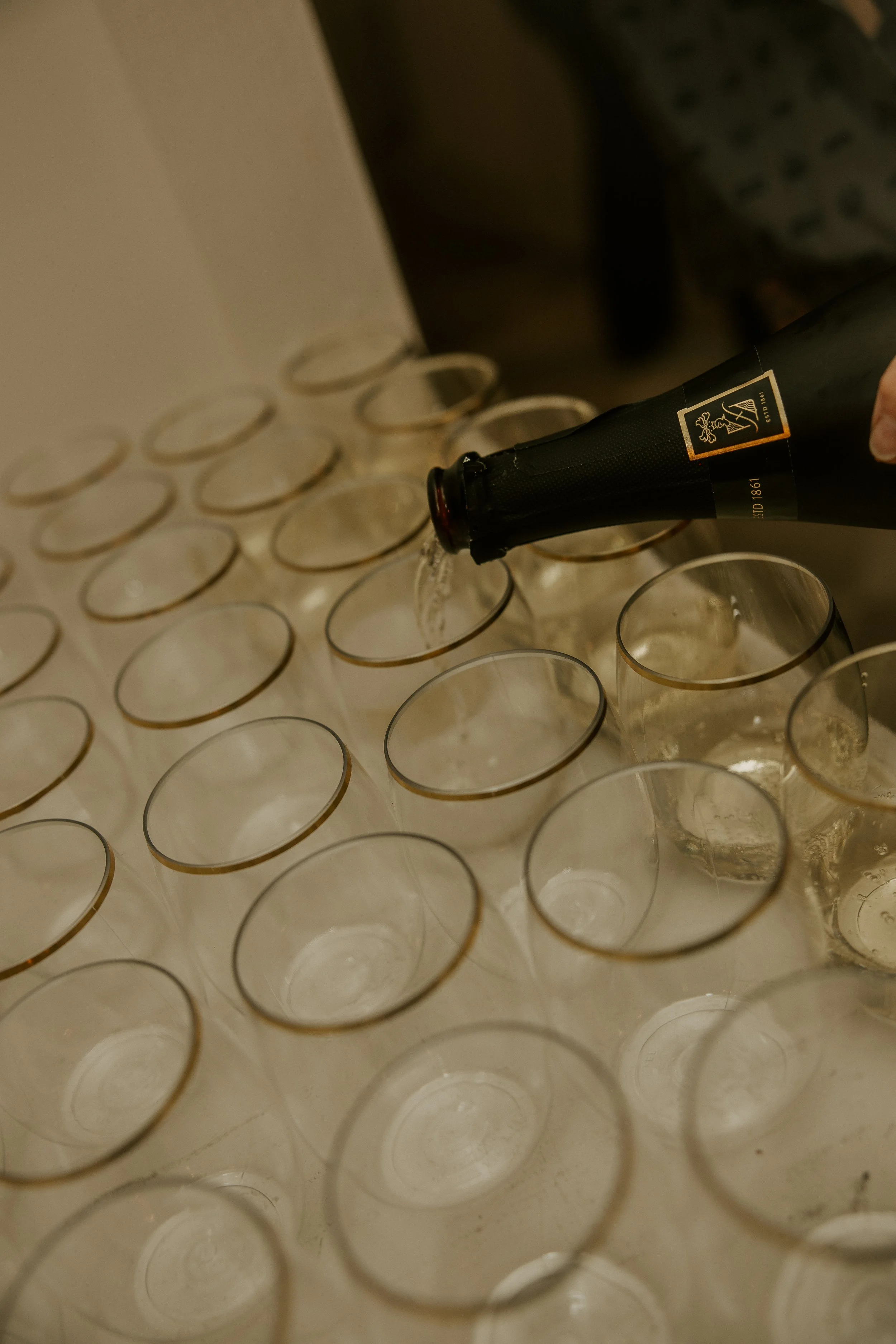 A person pouring champagne into a row of clear glasses.