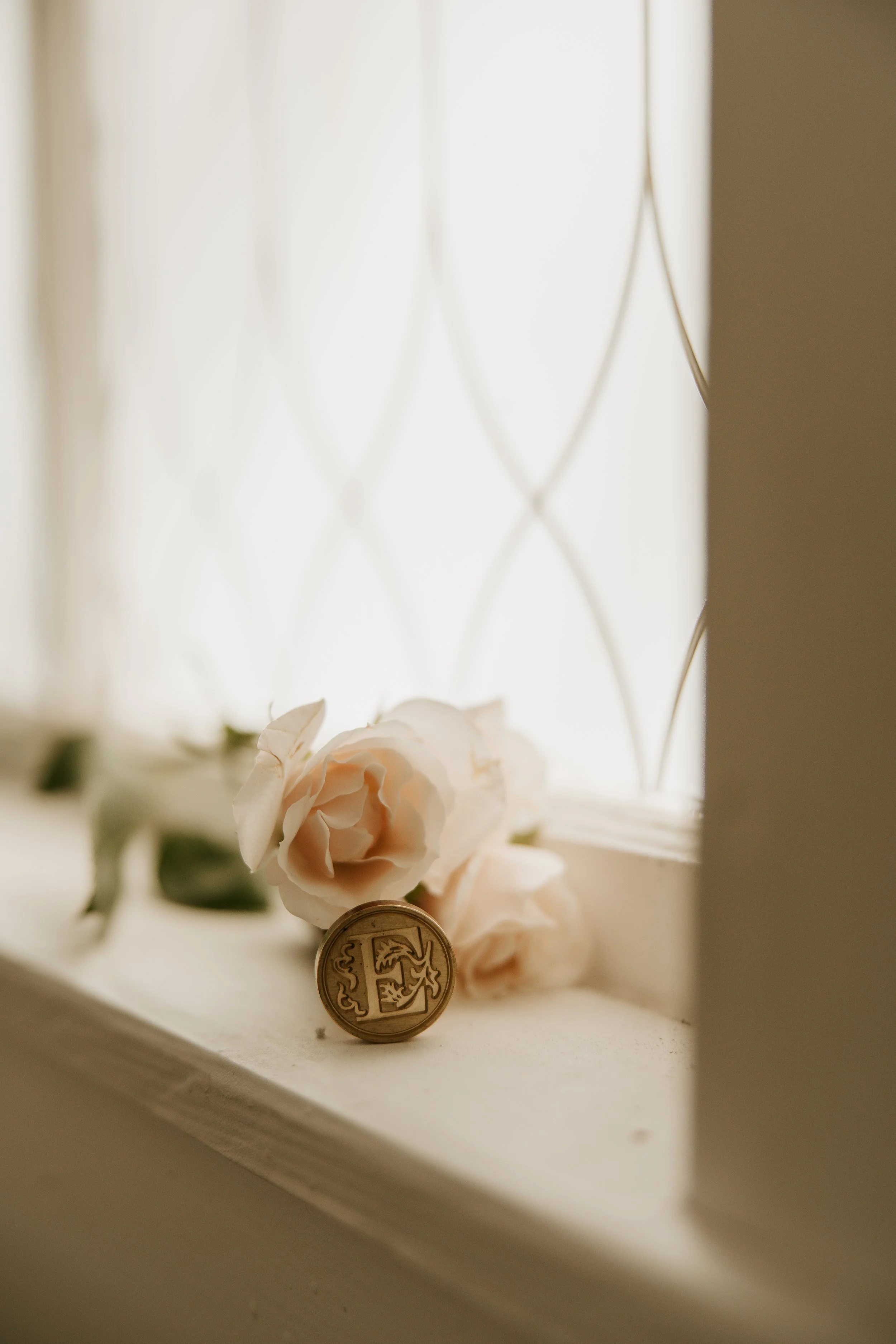 Soft pink roses and a coin resting on a windowsill near a decorative window grille with natural light