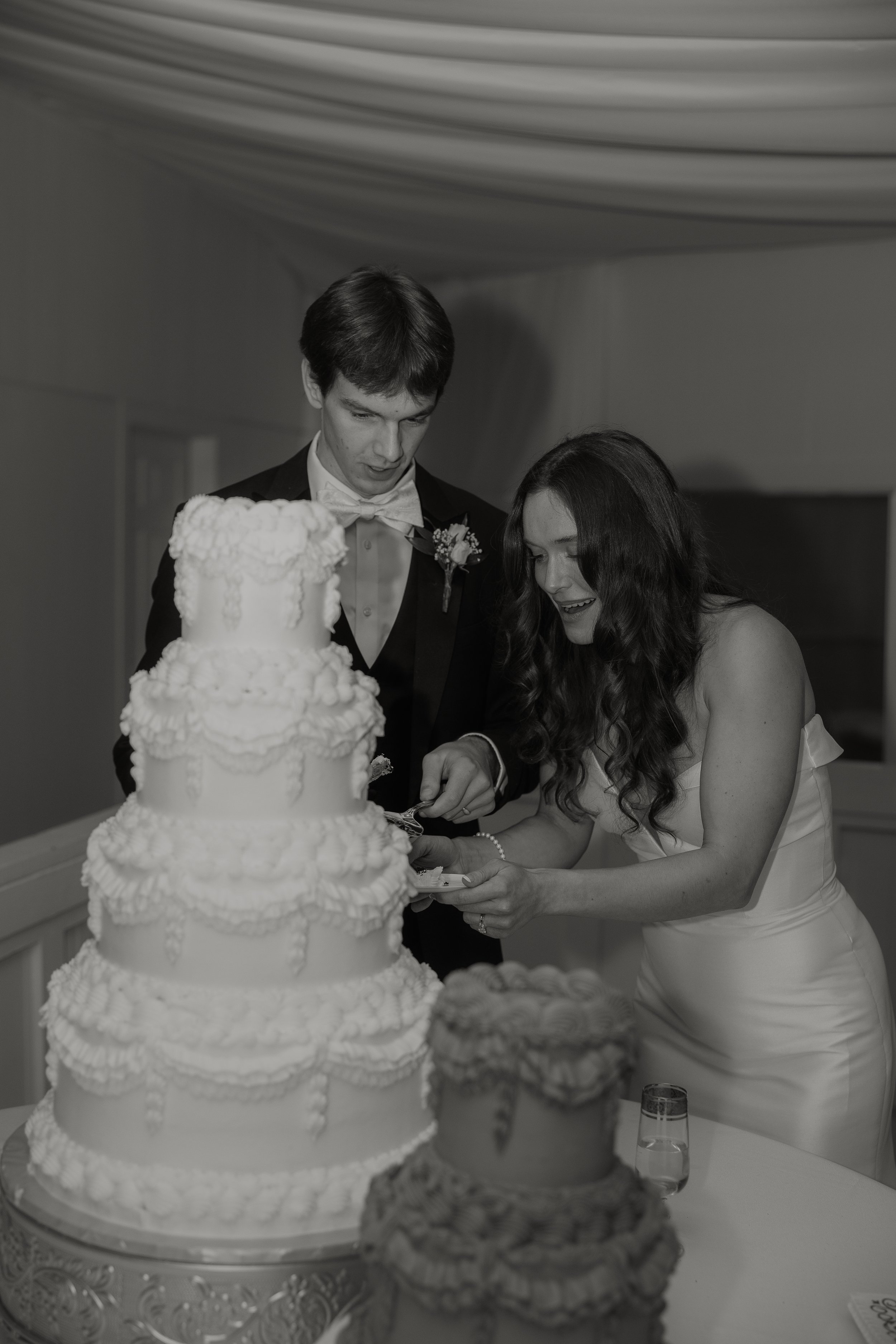 A black and white photo of a bride and groom cutting a wedding cake together.