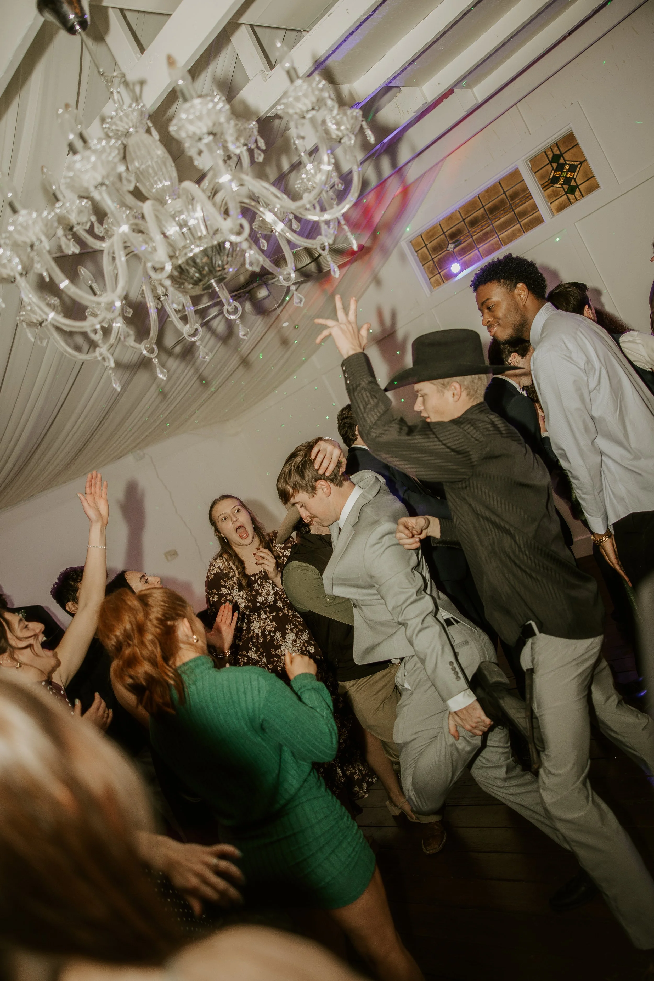People dancing and having fun at a party under a chandelier.