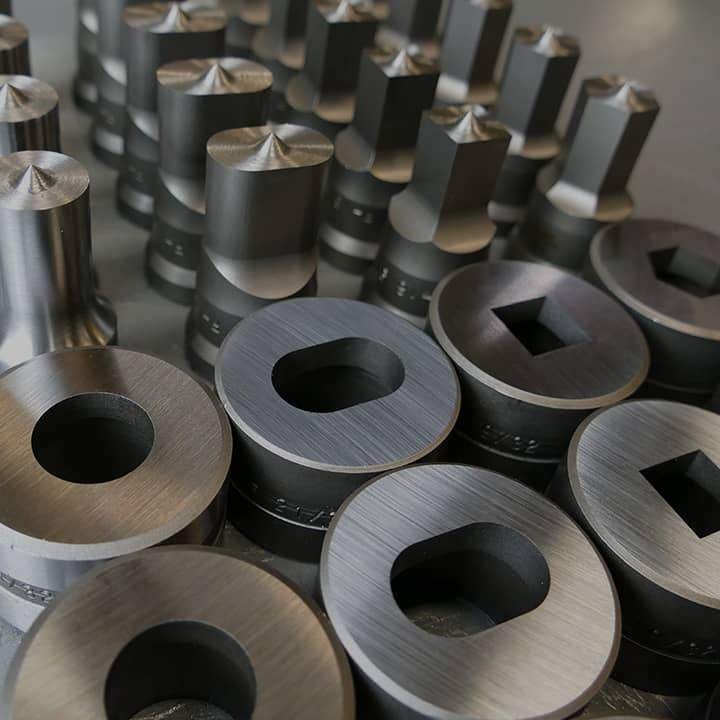 Collection of metallic machined components with circular and square holes arranged in rows.