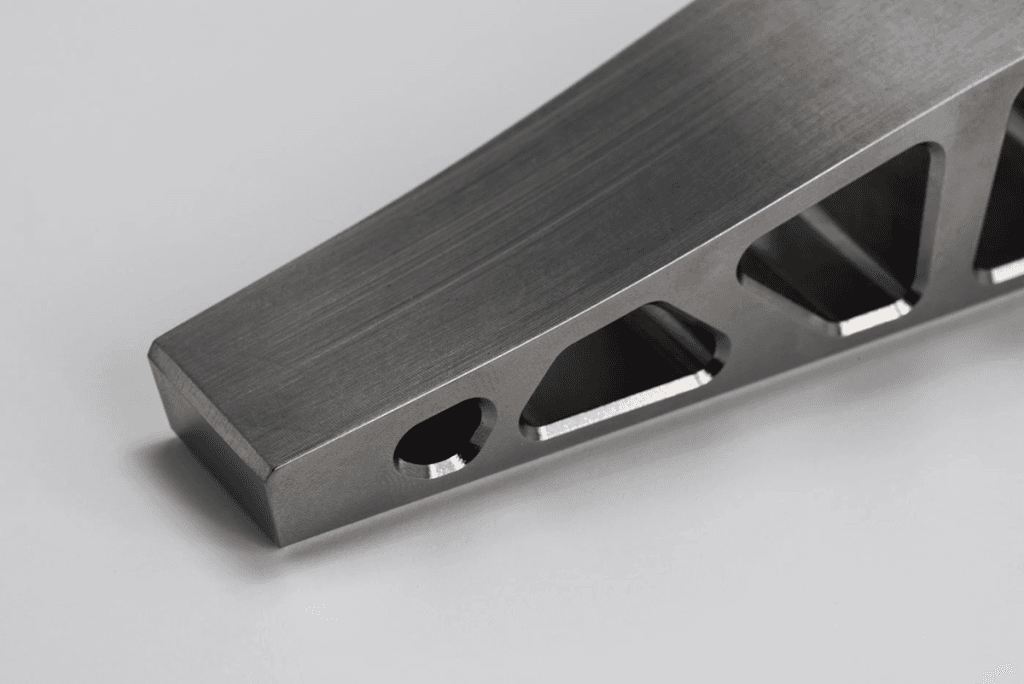 A close-up of a metallic triangular tool with a brushed finish, featuring circular and triangular cutouts along one edge.