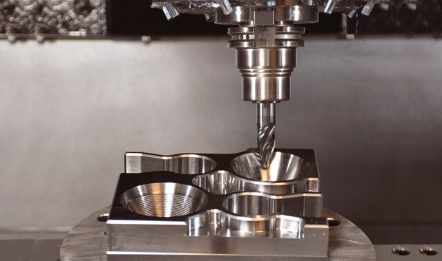 Close-up of a CNC machine with a drill bit cutting into a metal mold.