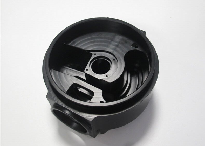 Black plastic or metal container with various internal compartments and openings, placed on a white surface.
