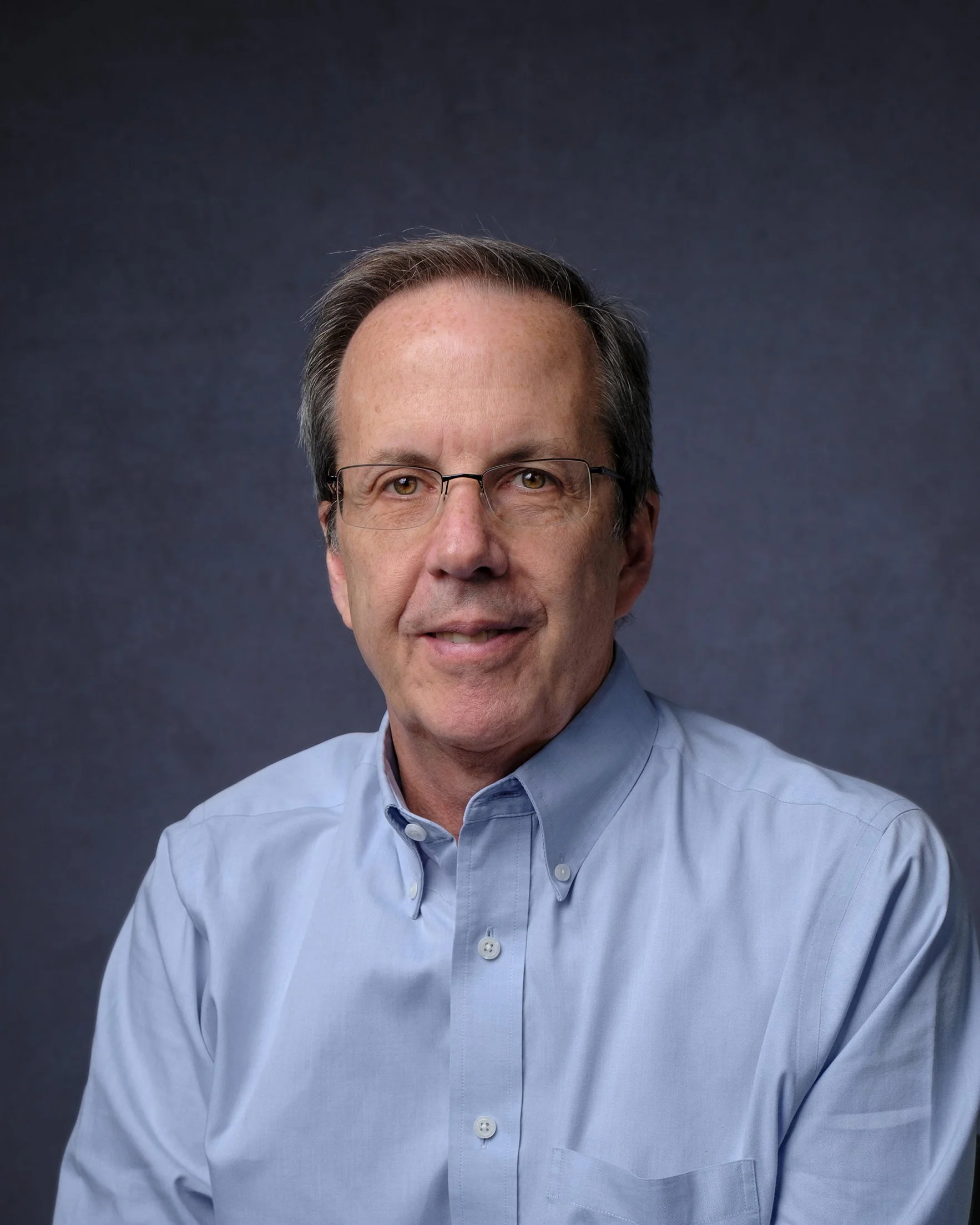 A headshot of Dr. Lee Harrison against a dark blue background