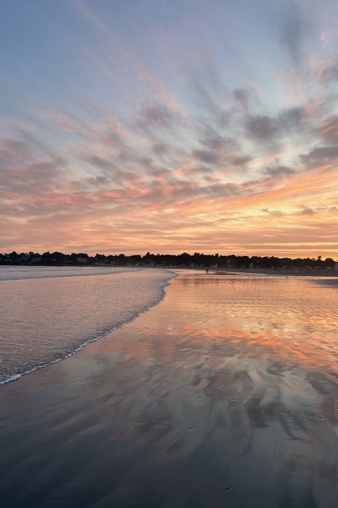 Colorful sunset over a calm beach with reflections on the wet sand and scattered clouds in the sky.