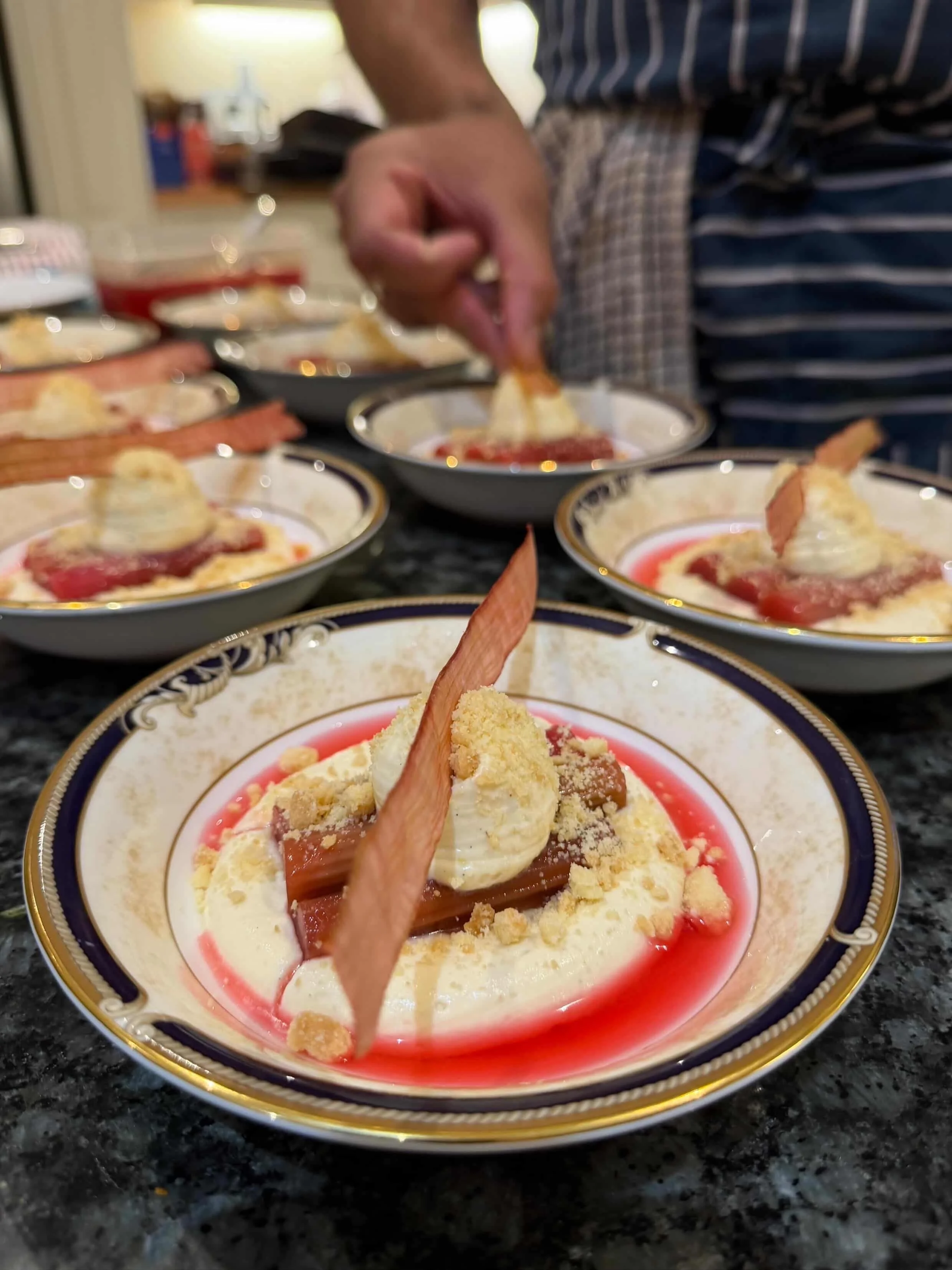 A close-up view of a plated dessert with vanilla ice cream, caramelized toppings, and a cookie wedge, garnished with a red syrup, on a decorative plate.